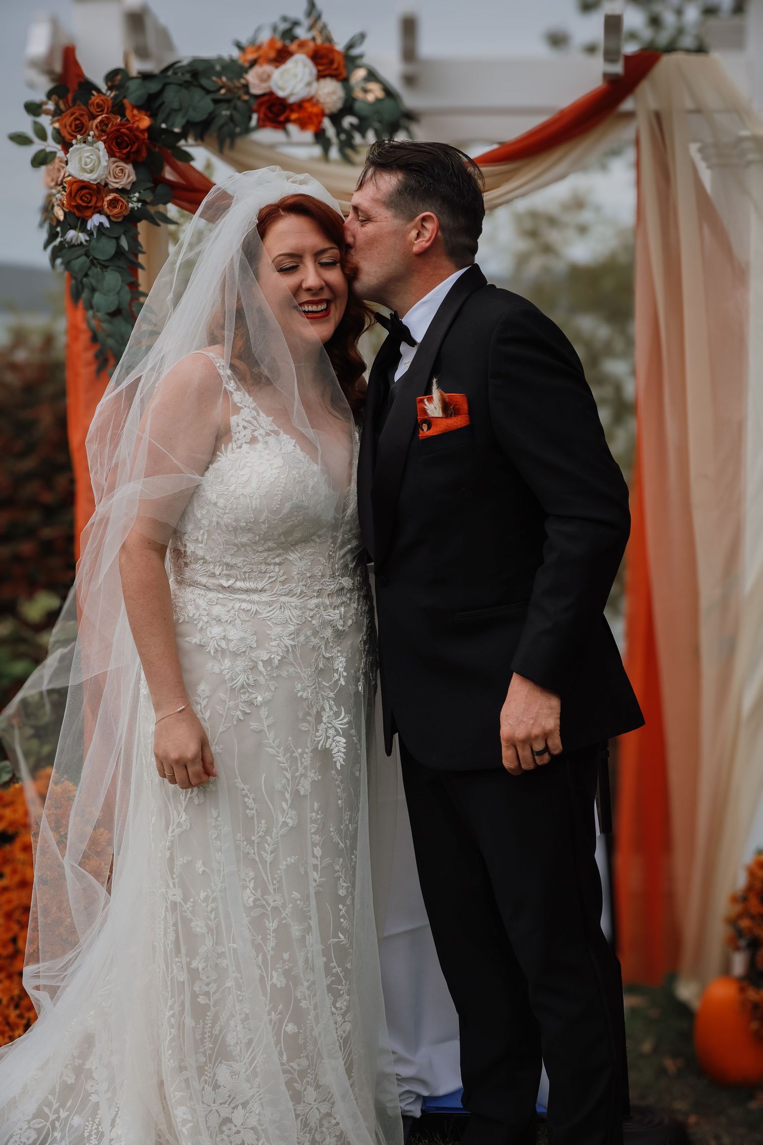 A romantic wedding couple shares tender moments in front of peach-colored drapery and autumn floral decorations.