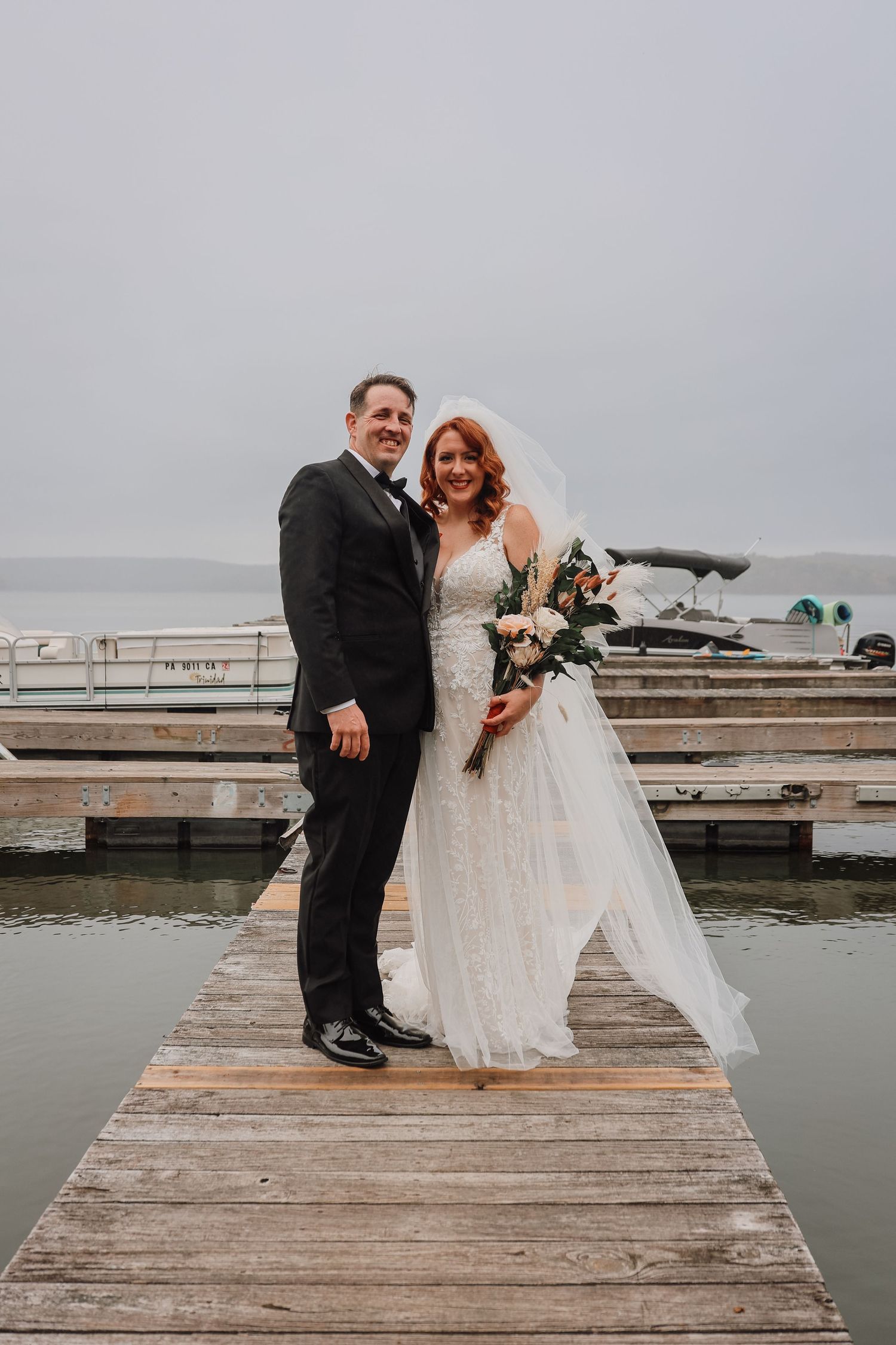 A couple in wedding attire shares intimate moments on a rustic wooden dock over misty water.