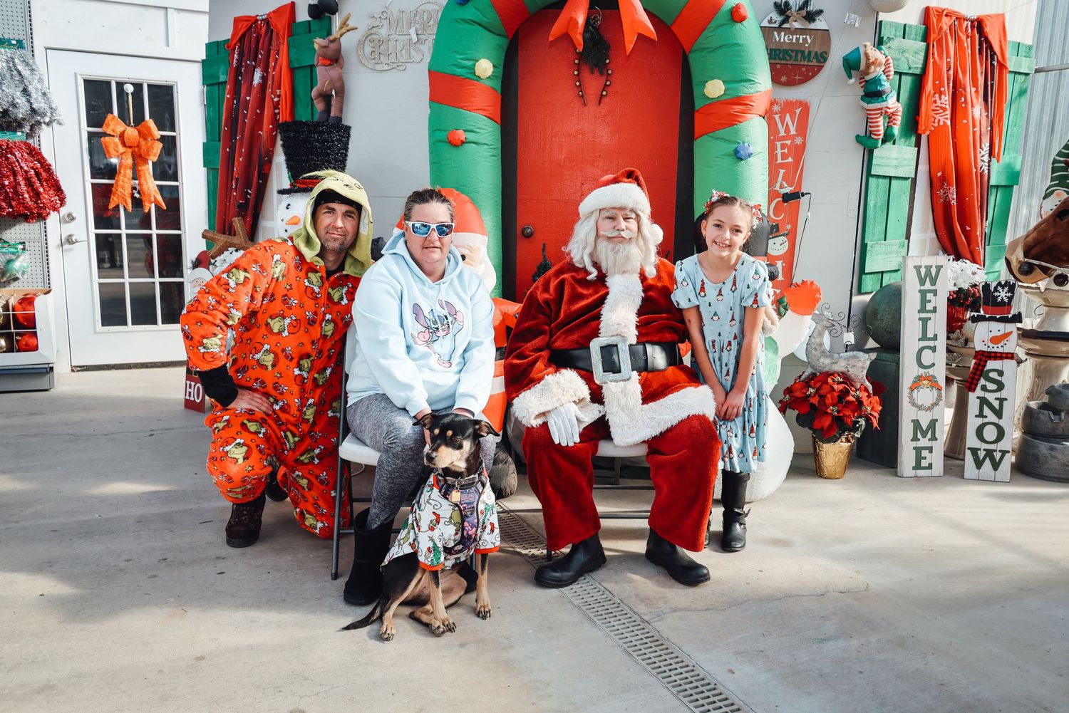 Festive holiday scene with people in red and green costumes posing together in front of a decorated storefront.