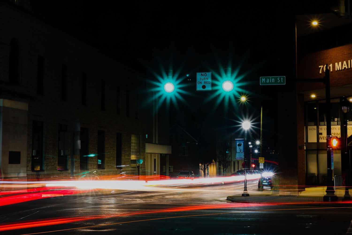 Long exposure night photograph of city street with green traffic lights and red light trails from passing cars.