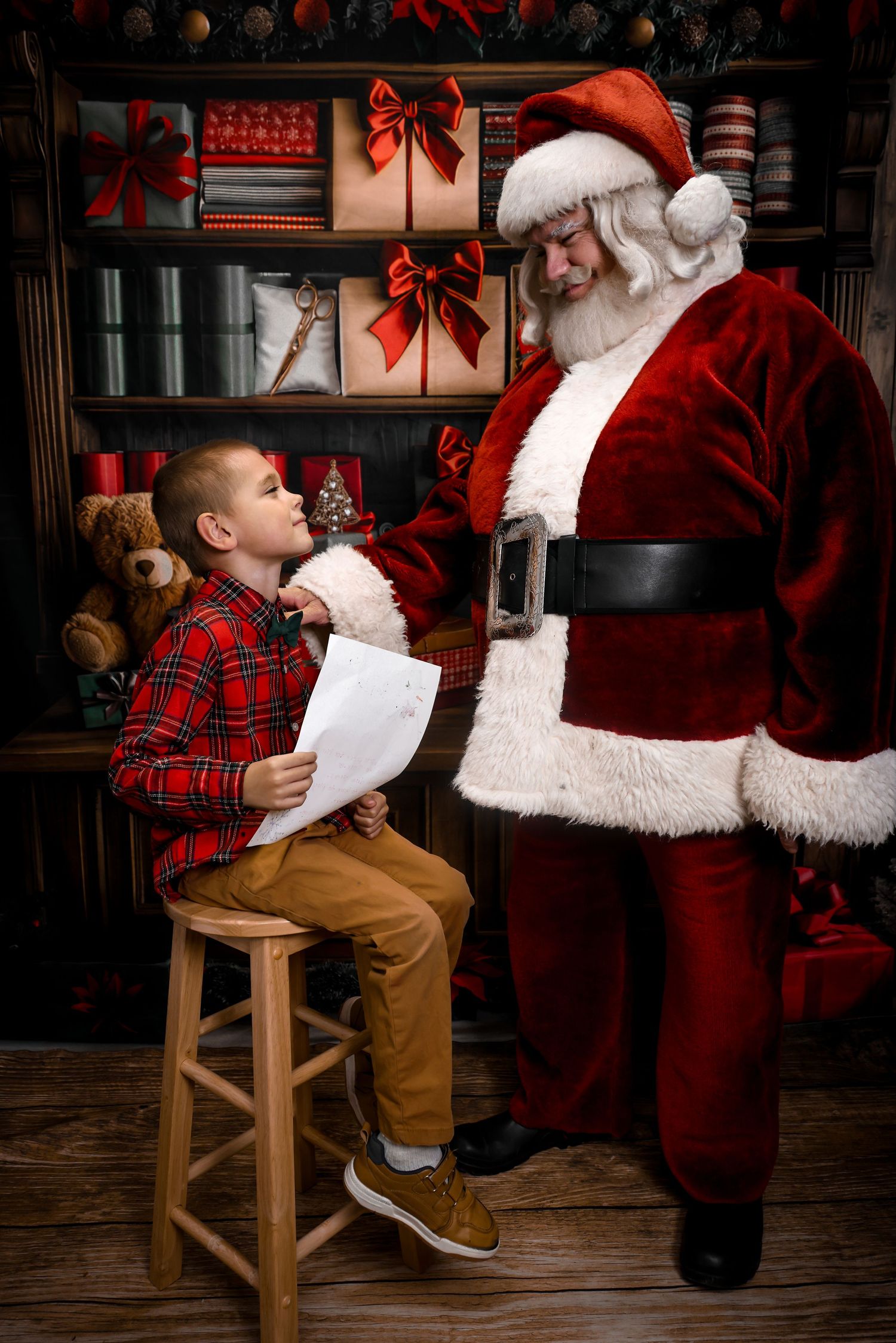 A magical Christmas scene shows a child in plaid sitting on a wooden stool while visiting with Santa Claus.