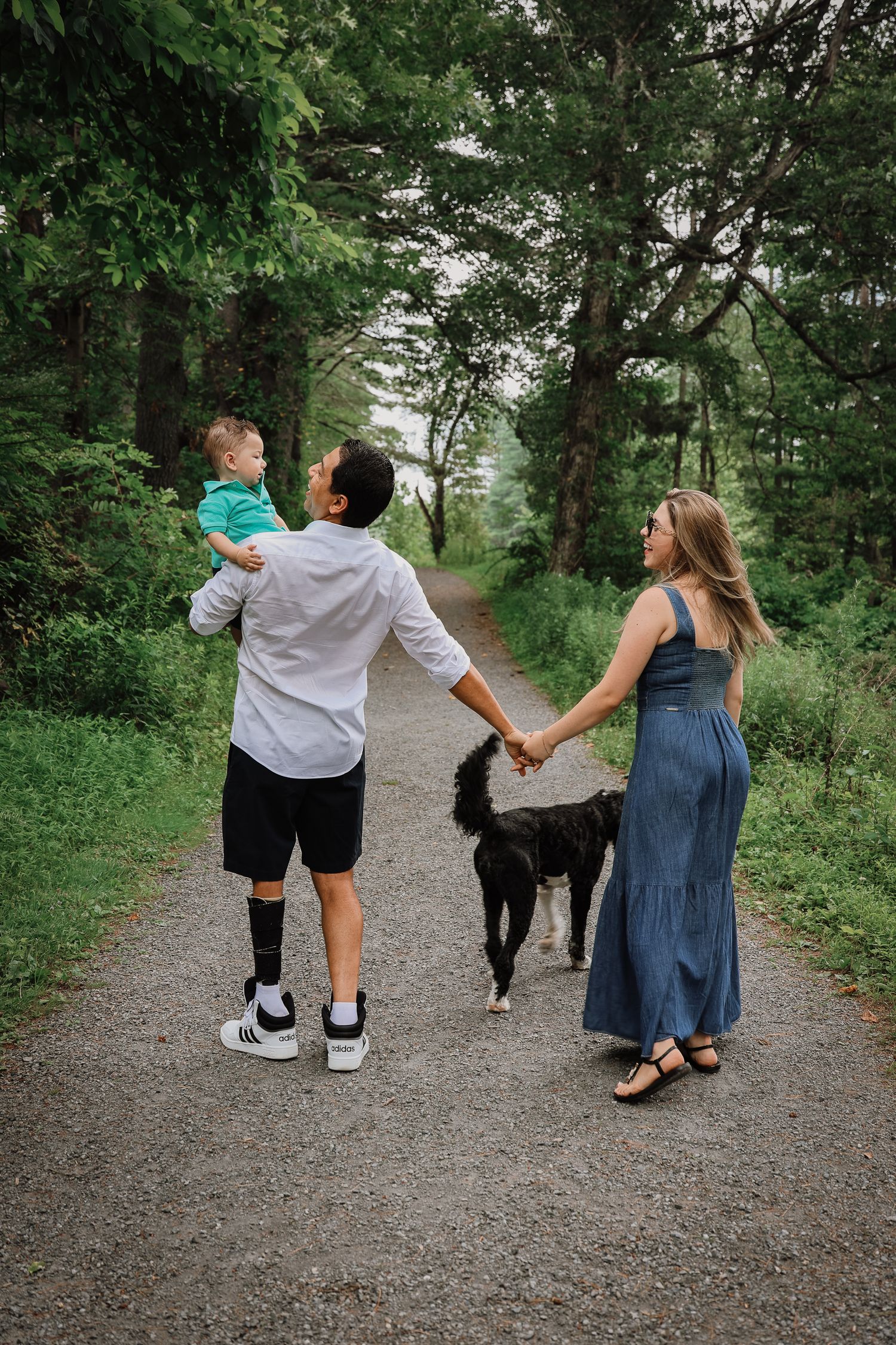 A group walks together holding hands on a peaceful wooded trail surrounded by lush green foliage.