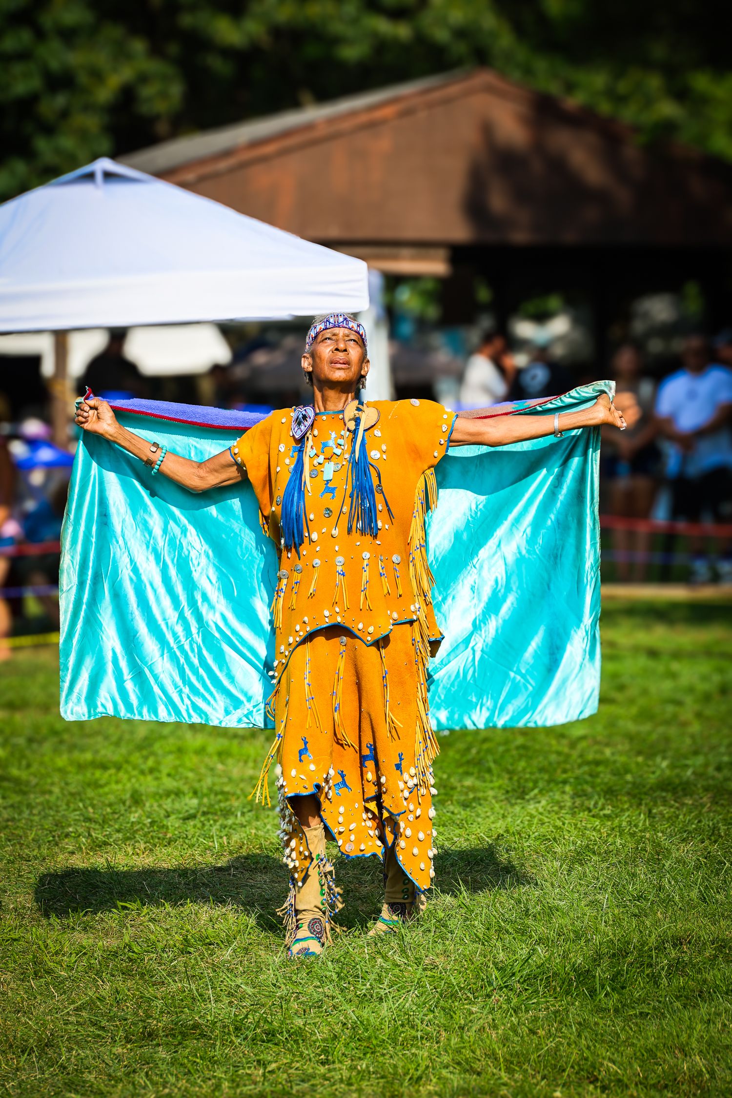 Native American dancer performs traditional dance wearing vibrant gold regalia with turquoise wings on grassy field.
