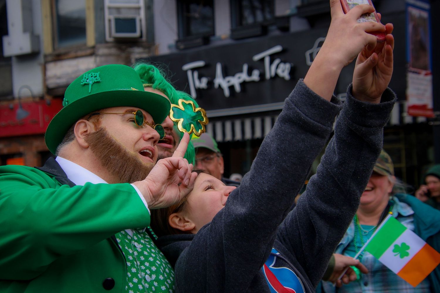 Crowds celebrate St Patrick's Day with Irish flags and green attire while cheering in the streets.