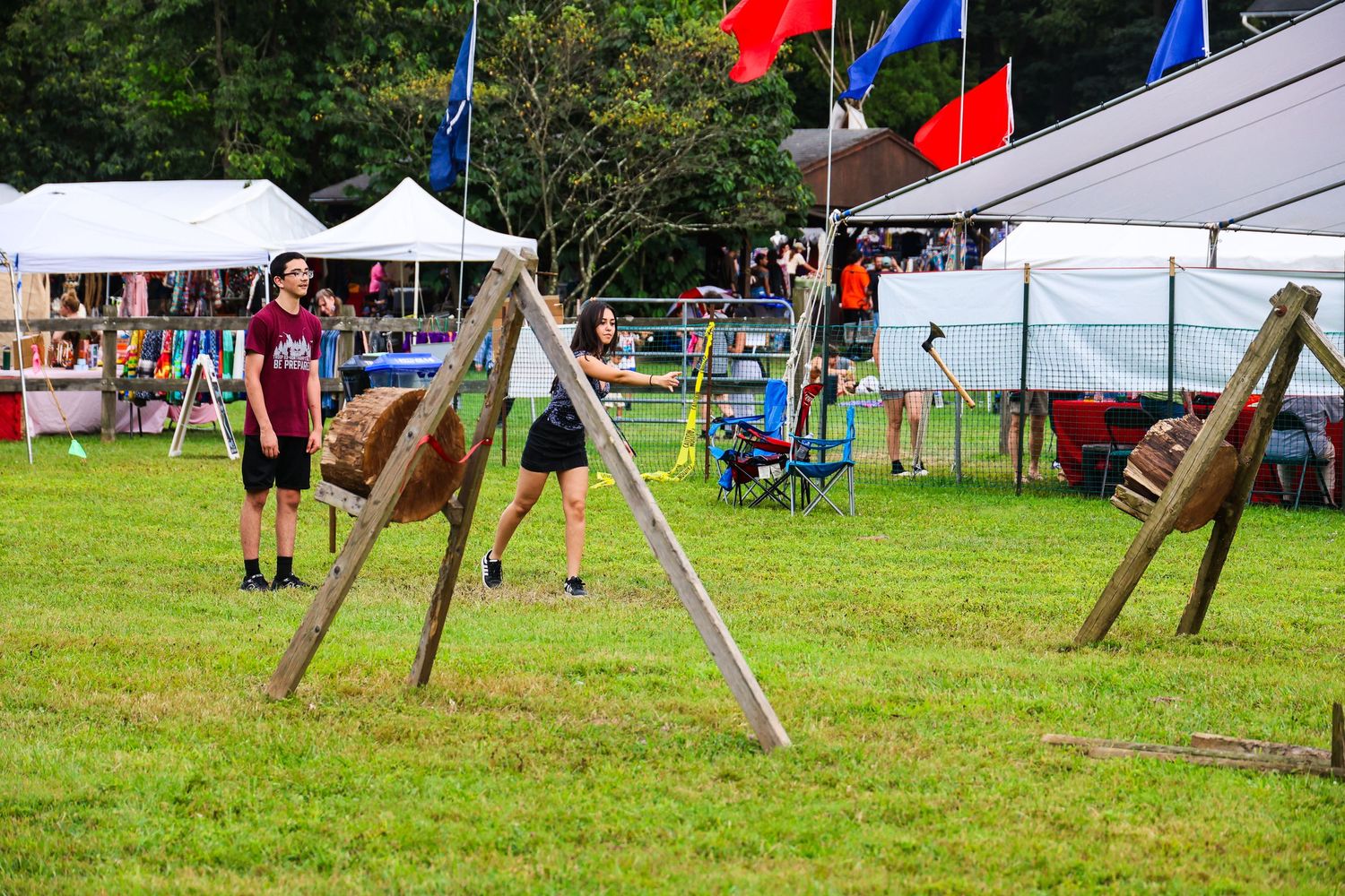Volleyball players compete in an outdoor grass court match with colorful flags and tents visible in the background.