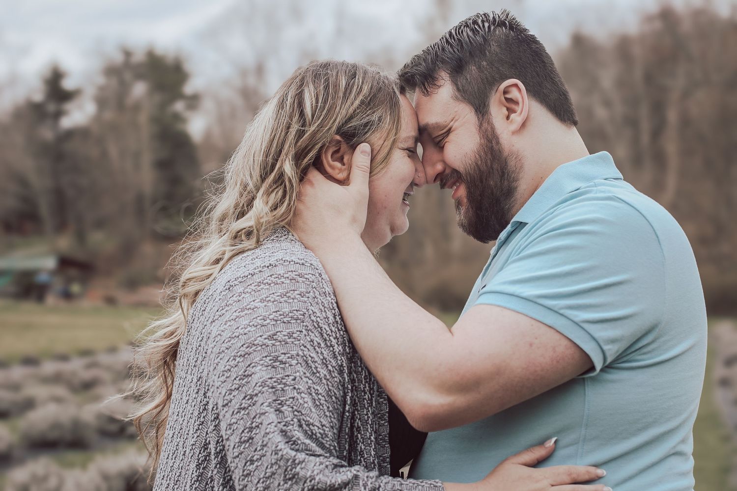 A romantic couple embraces outdoors in a natural setting during an engagement photo session.