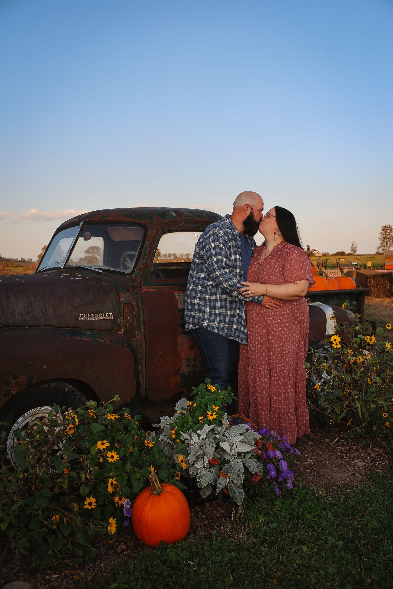 A rustic vintage truck surrounded by blooming sunflowers and pumpkins creates a romantic autumn scene at sunset.
