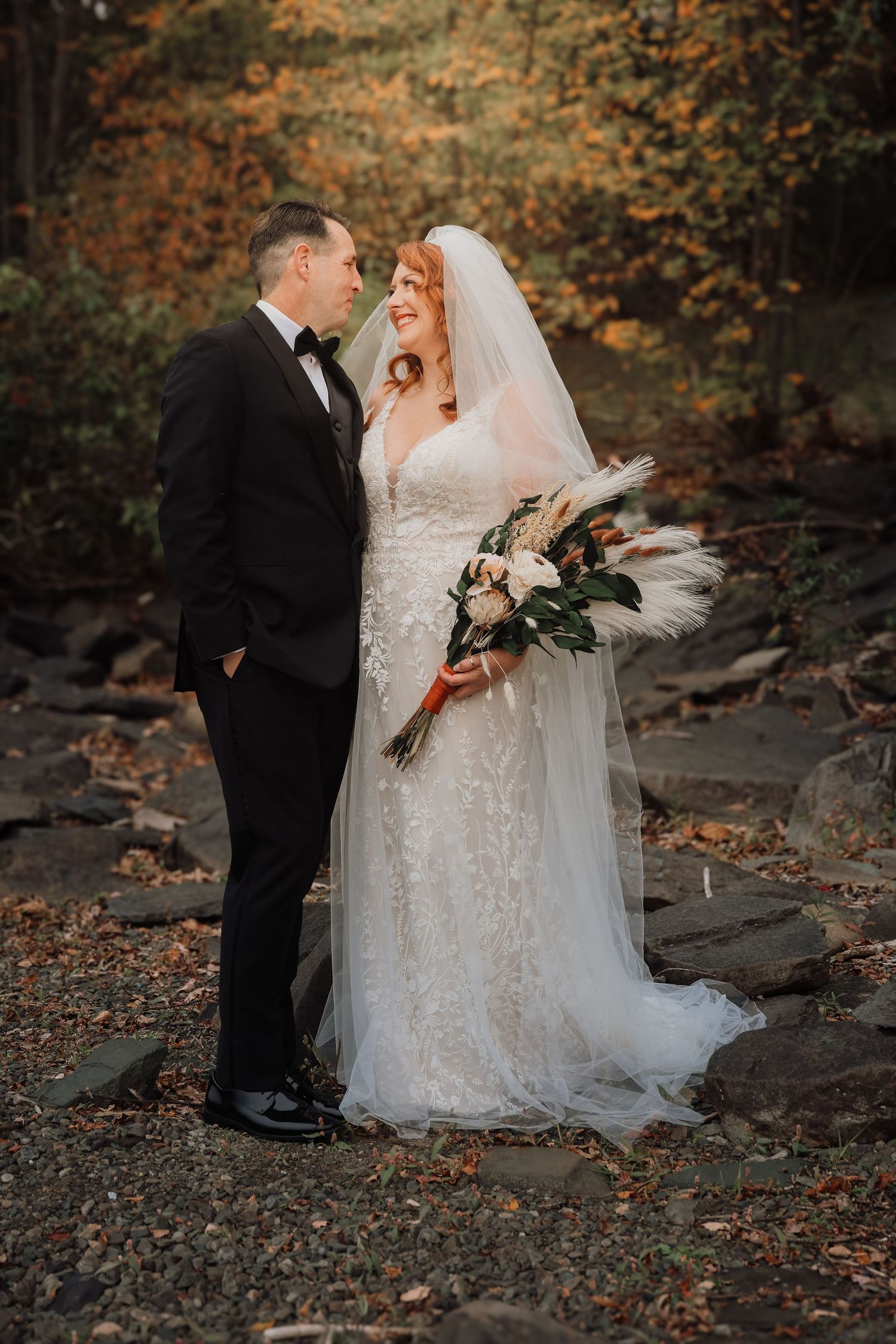 Romantic wedding couple poses on rocky terrain surrounded by autumn foliage.