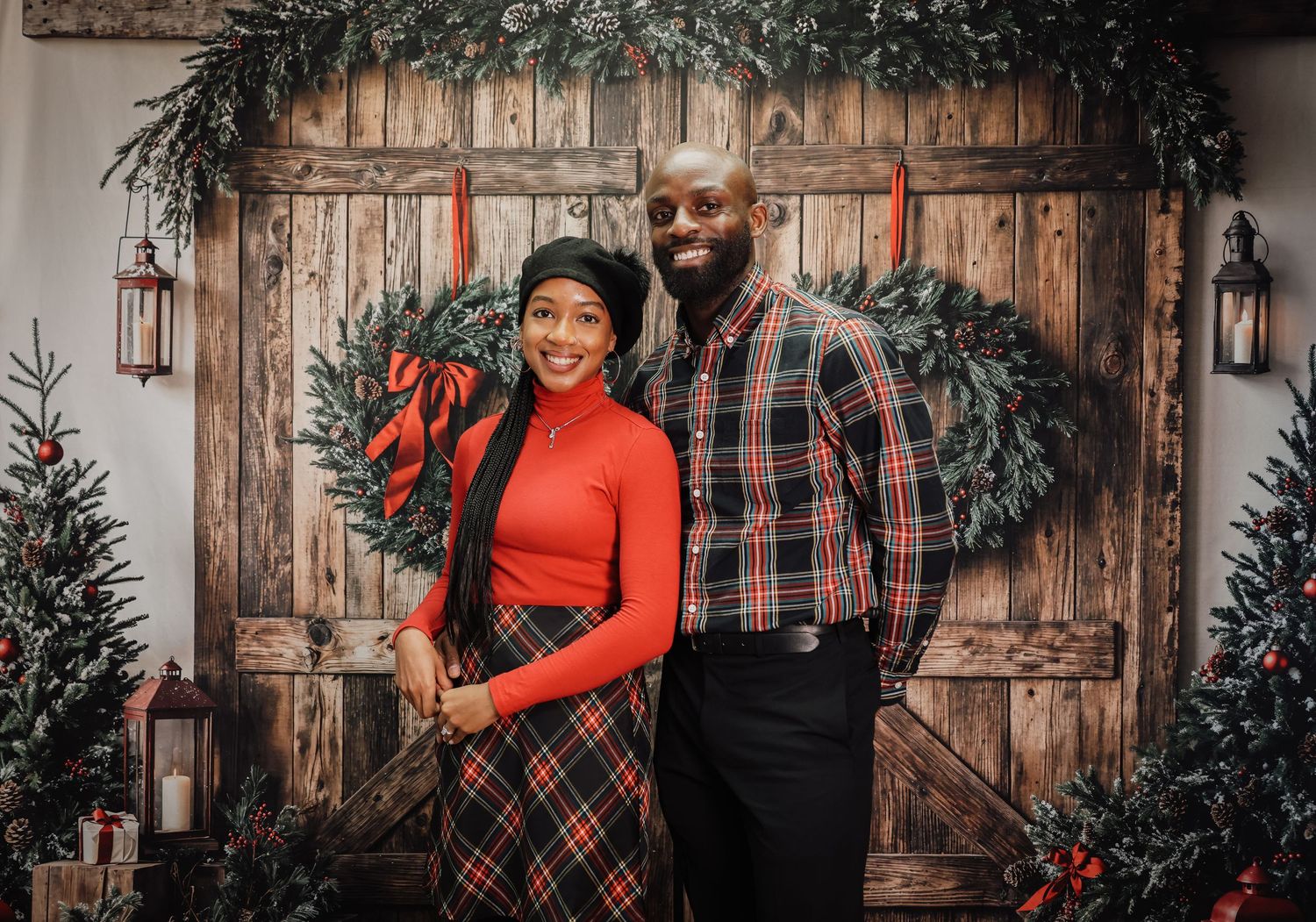 Romantic winter holiday photoshoot with couple embracing in front of rustic wooden door with Christmas decor.