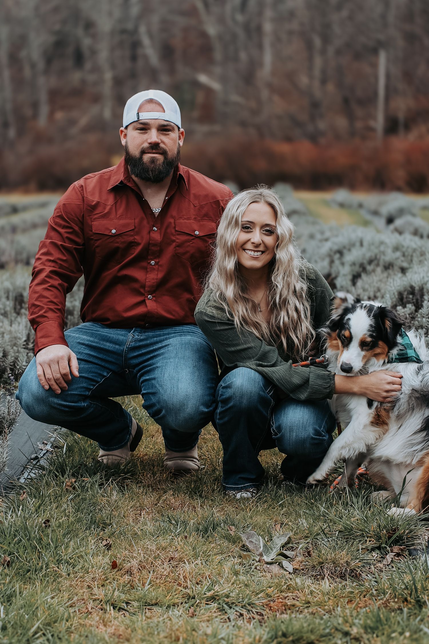 A couple sits on mossy rocks with their Australian Shepherd dog during an outdoor photo session.