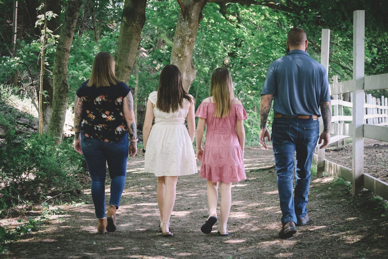 A group of people walk along a shaded garden path lined with trees and greenery.