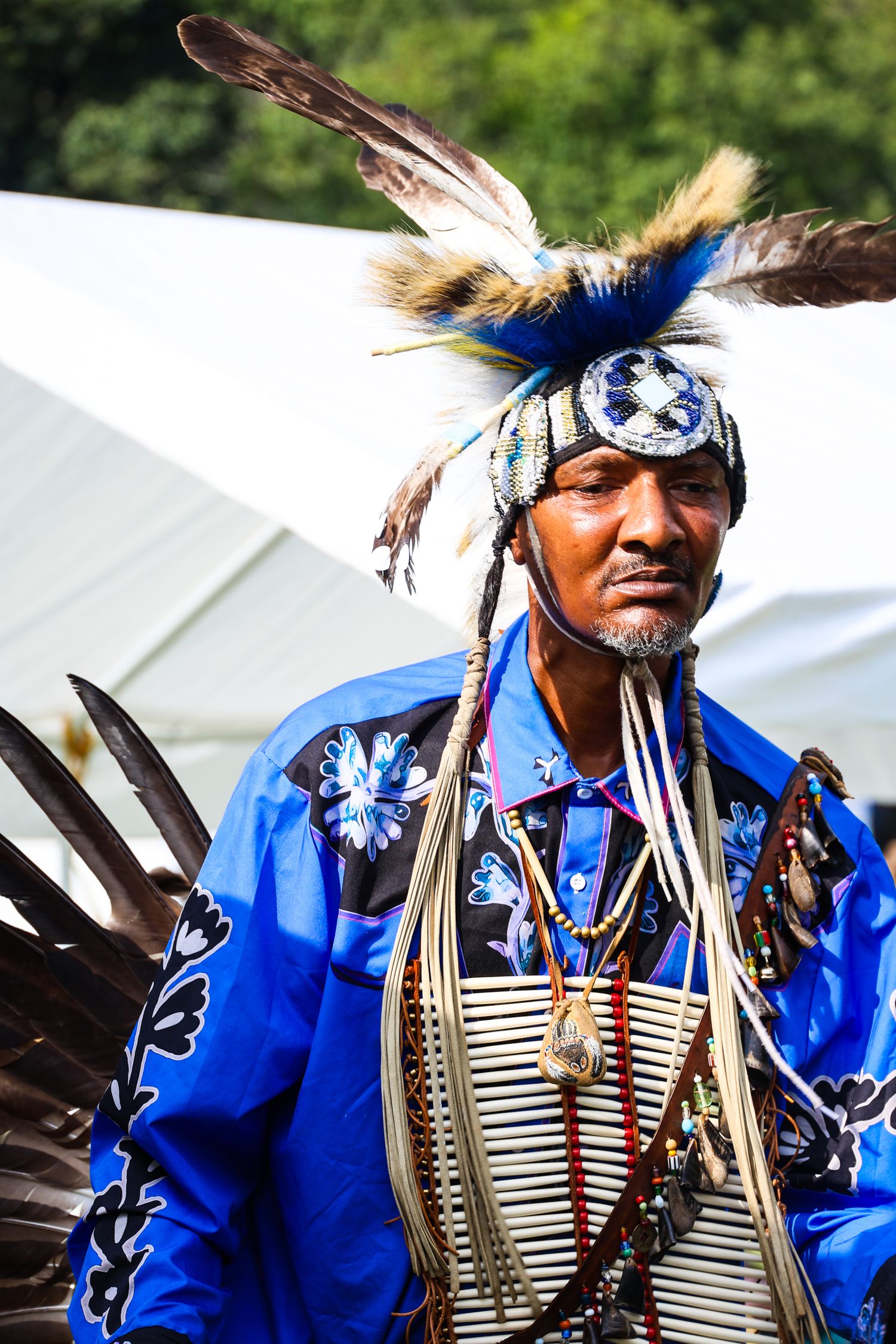 Traditional Native American dancer wearing blue regalia with feathers and beadwork performs at cultural festival.