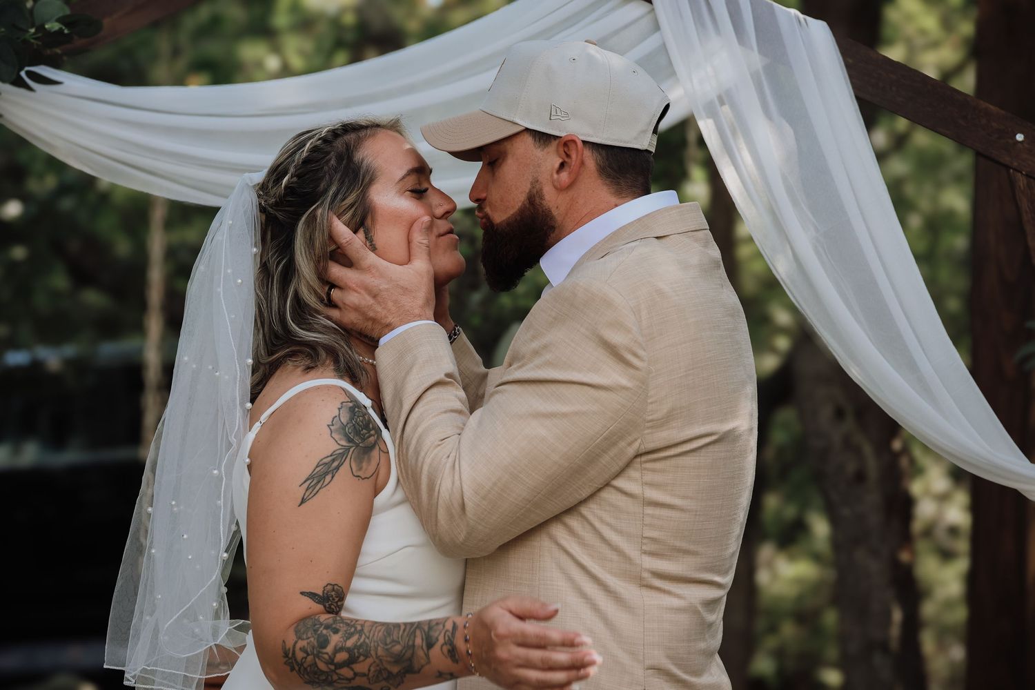An intimate wedding photo sequence showing a couple sharing tender moments under white fabric draped between trees.