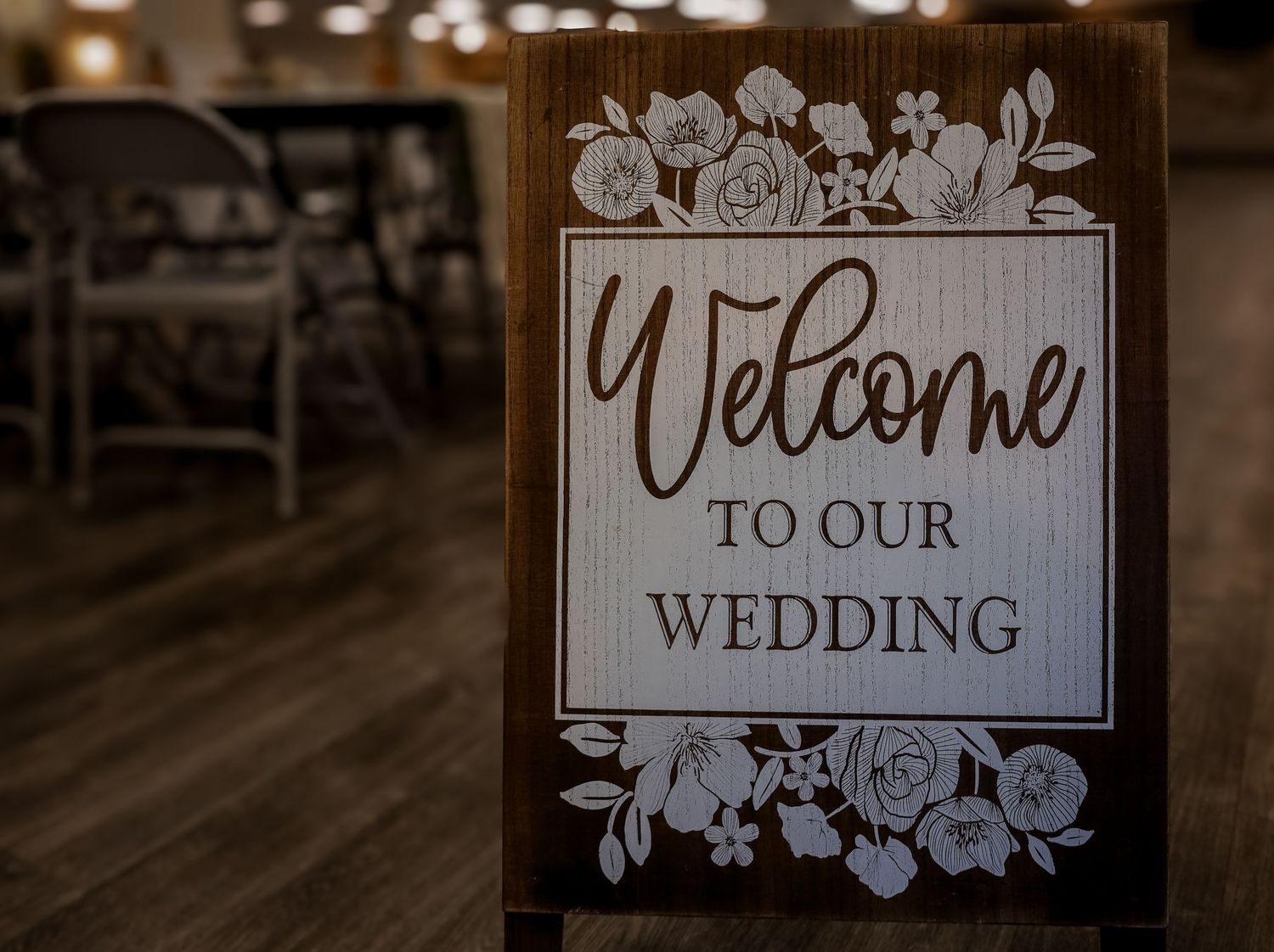 Elegant wedding welcome signs with floral designs displayed on wooden easels at a rustic venue.