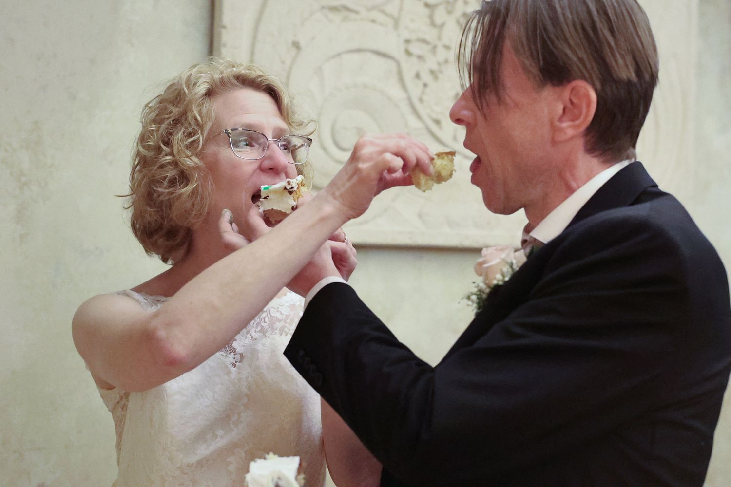 A bride and groom playfully feed each other wedding cake during their reception celebration.