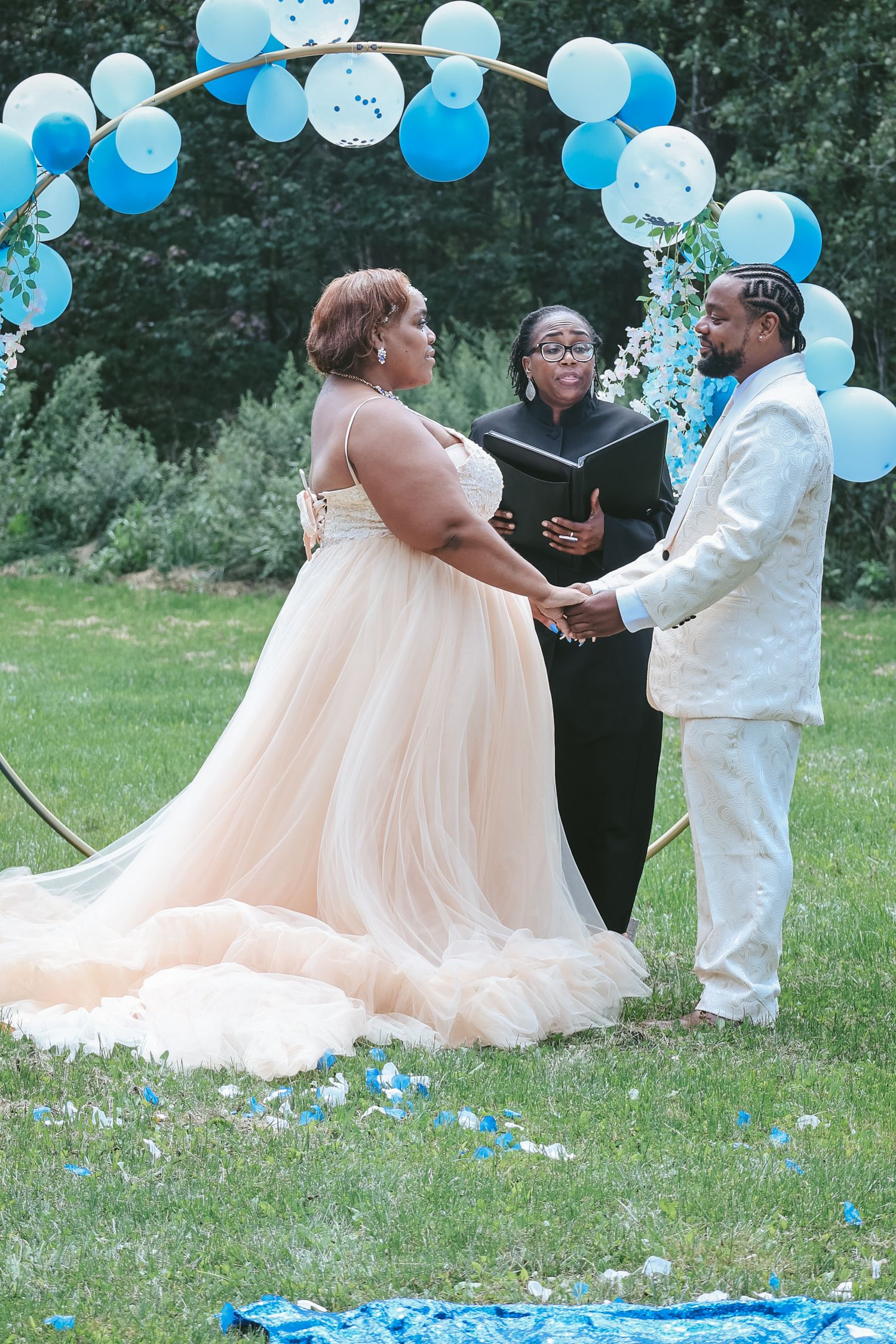 A wedding ceremony takes place outdoors with light blue balloons decorating the scene as a couple exchanges vows.