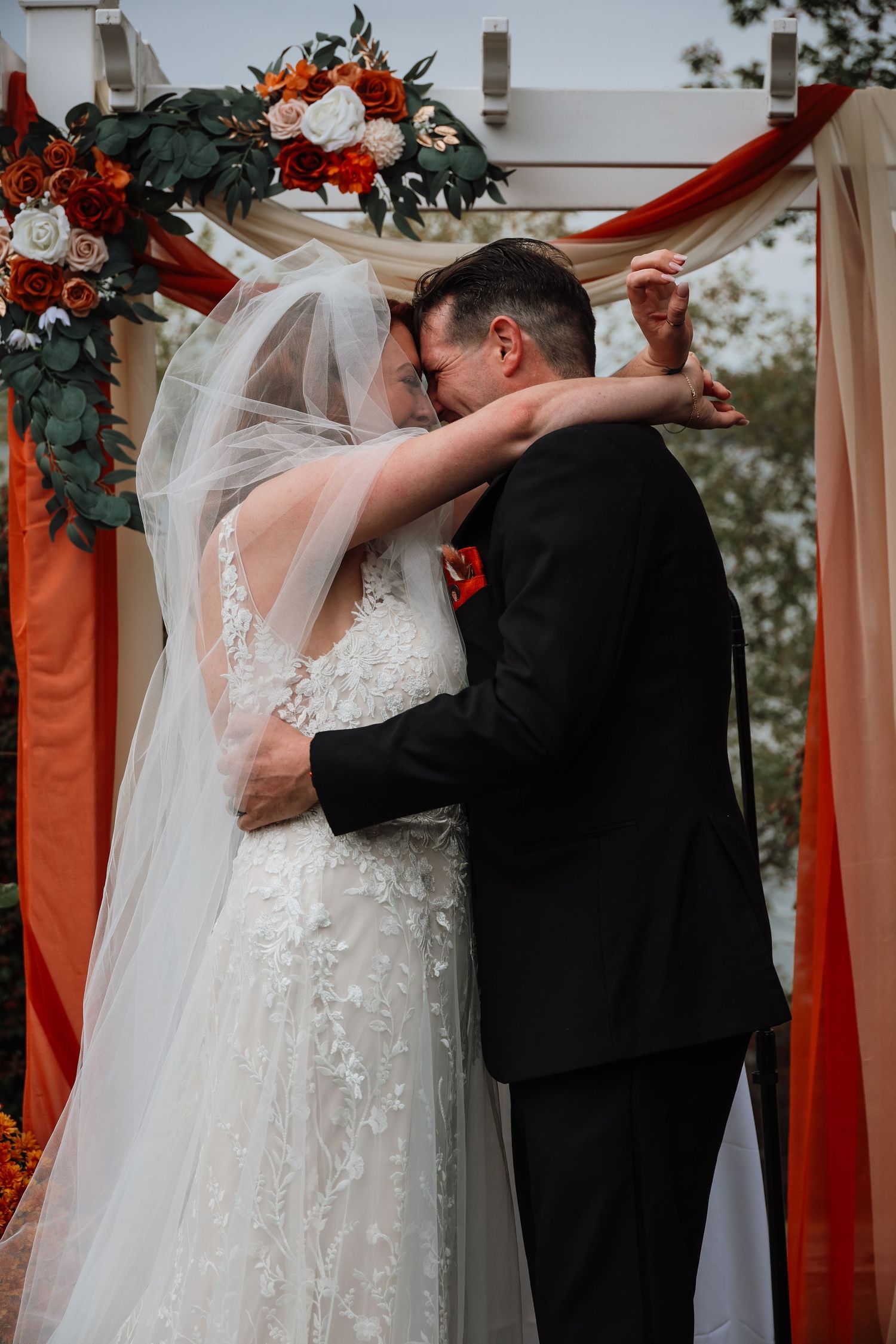 A romantic wedding ceremony under a red draped arch decorated with lush florals and greenery.