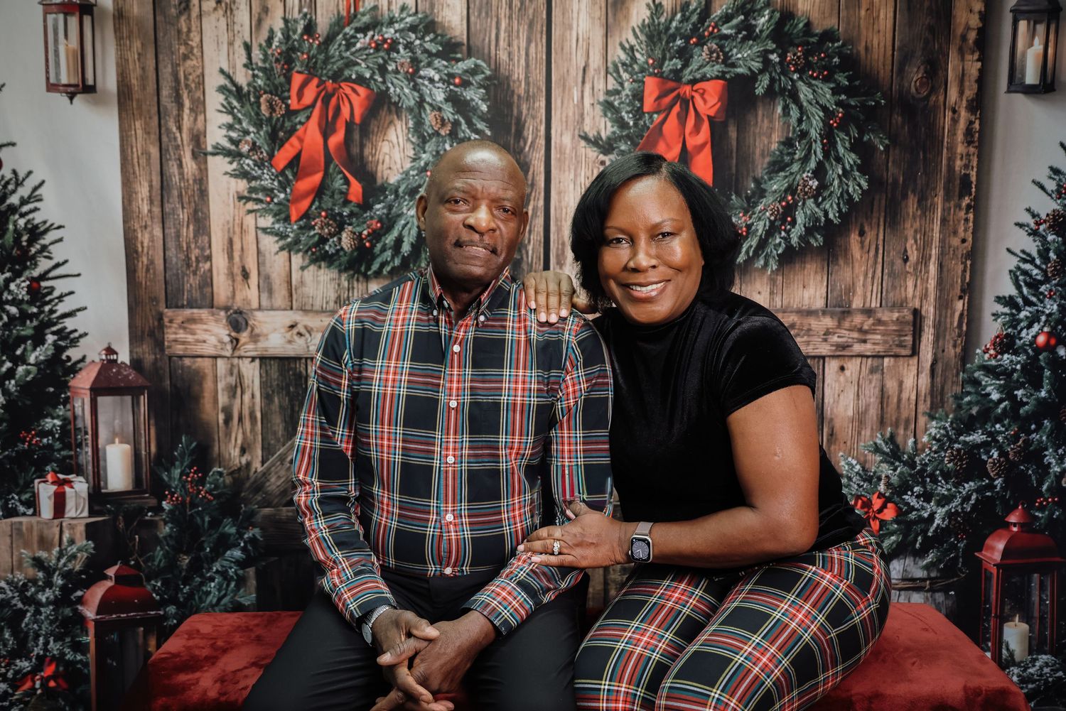 A couple poses together for holiday photos in front of a rustic wooden backdrop with festive Christmas decorations.