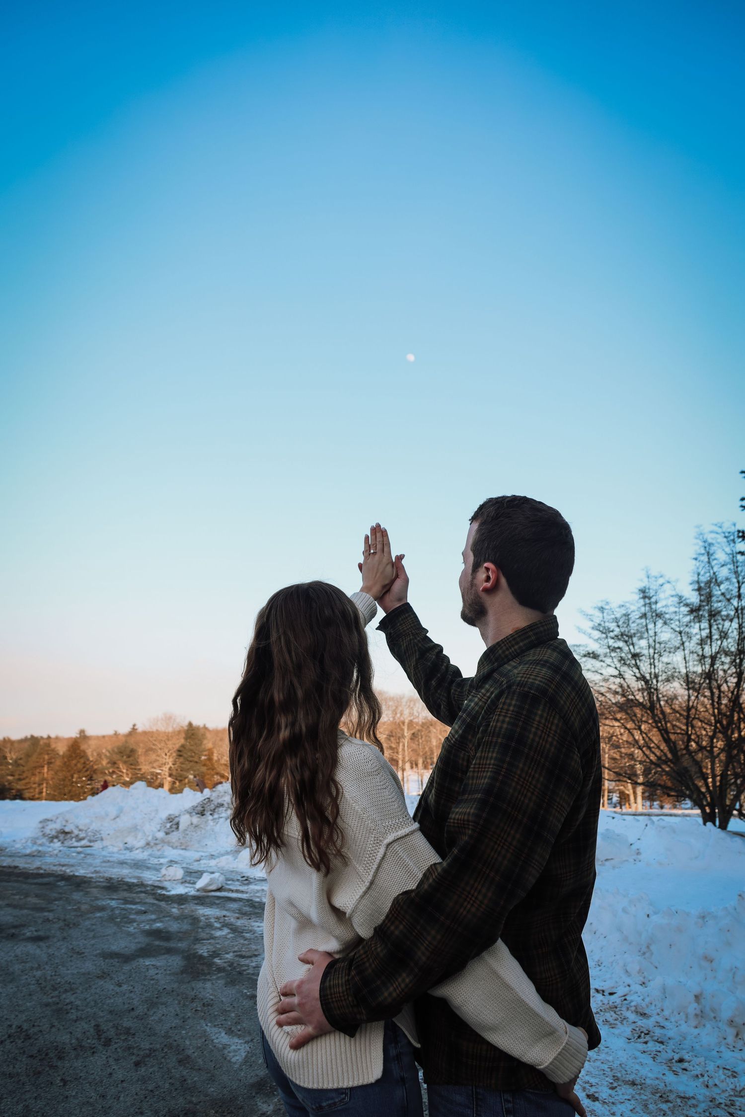 A couple in winter attire sharing a high five against a snowy landscape and blue sky at sunset.