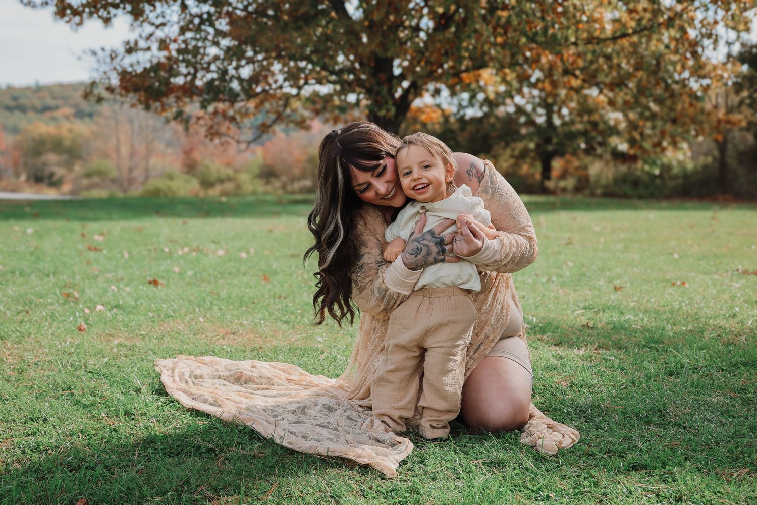 A mother and child share tender moments together on a grassy field during an autumn day.