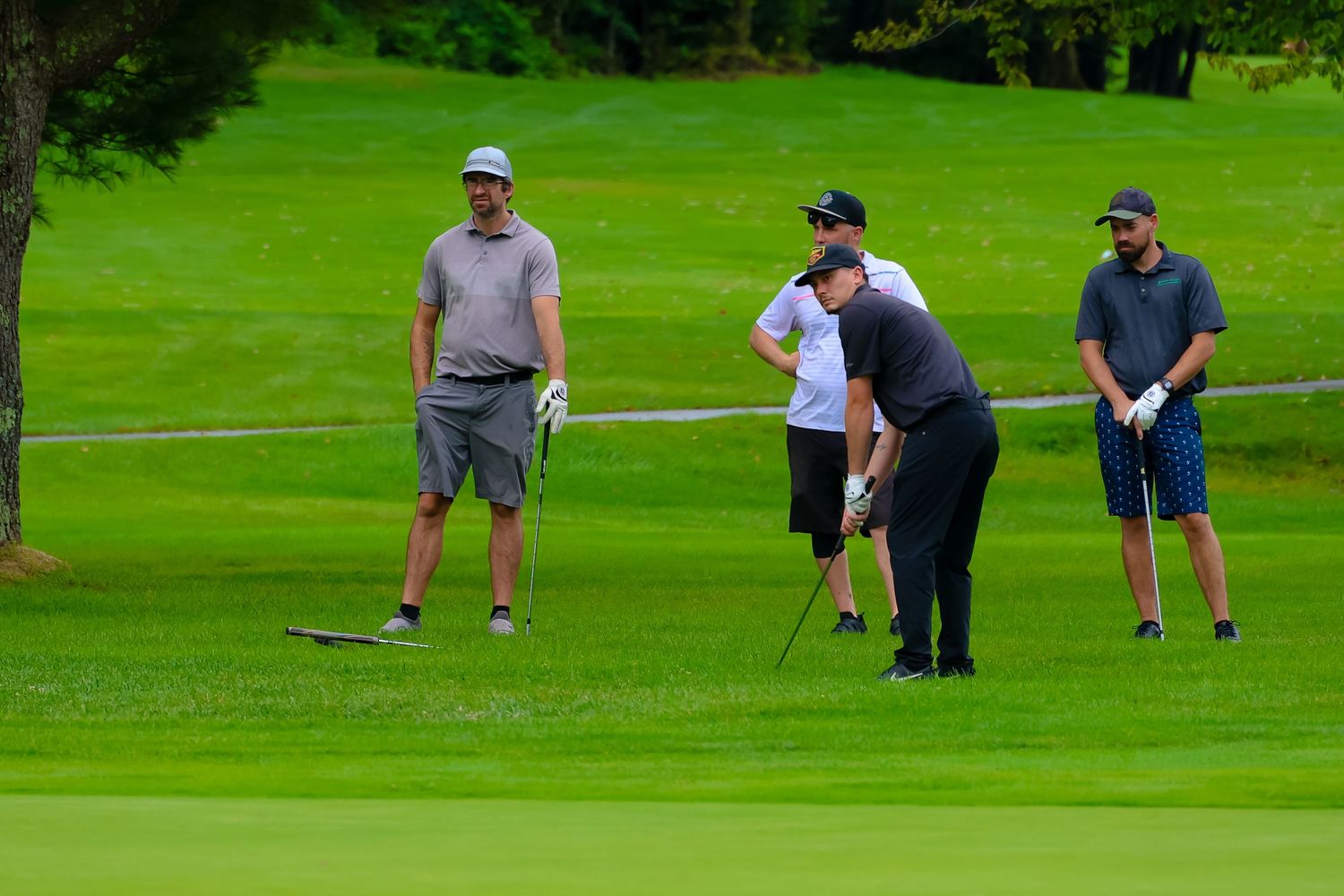 Golfers practice putting on a lush green course while others observe their technique on a sunny day.