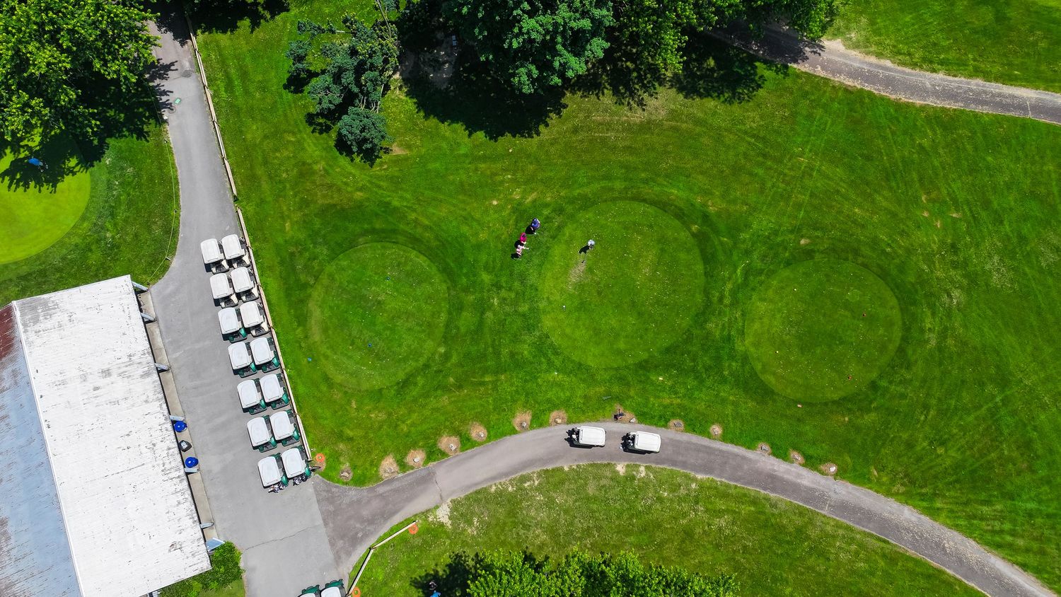 Aerial view of a green golf course with white golf carts parked near a clubhouse and winding paths.