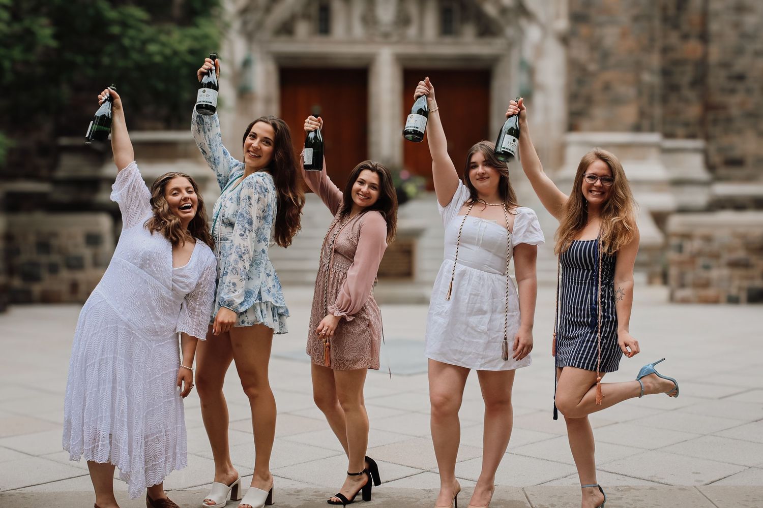 Group of friends in casual summer outfits pose together on stone steps during a sunny outdoor photoshoot.