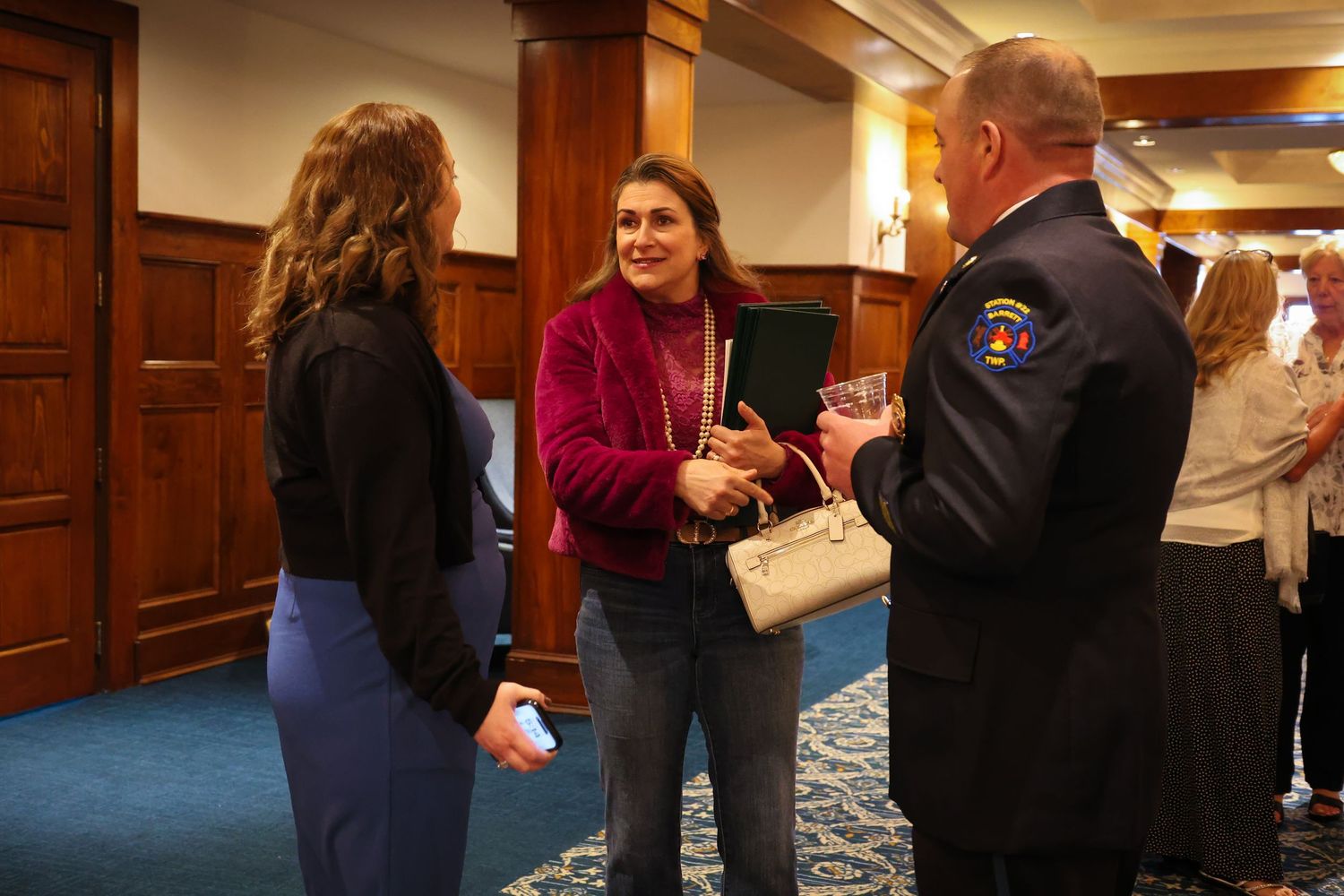 People gathered in a carpeted hallway with wood paneling and warm lighting having conversations.