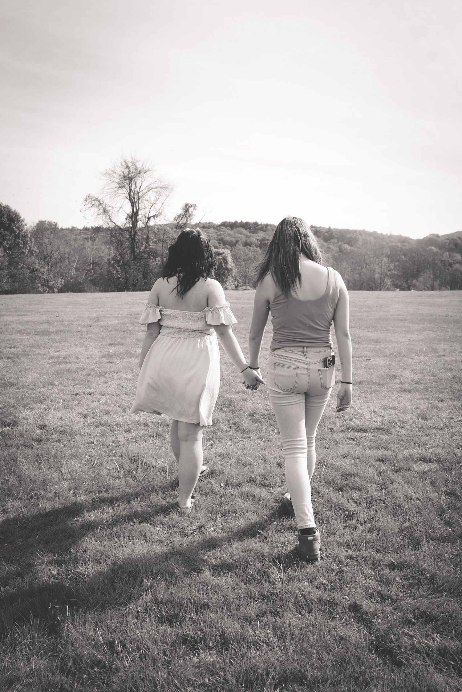 Two people walking hand in hand through a grassy field on a cloudy day, captured in black and white.