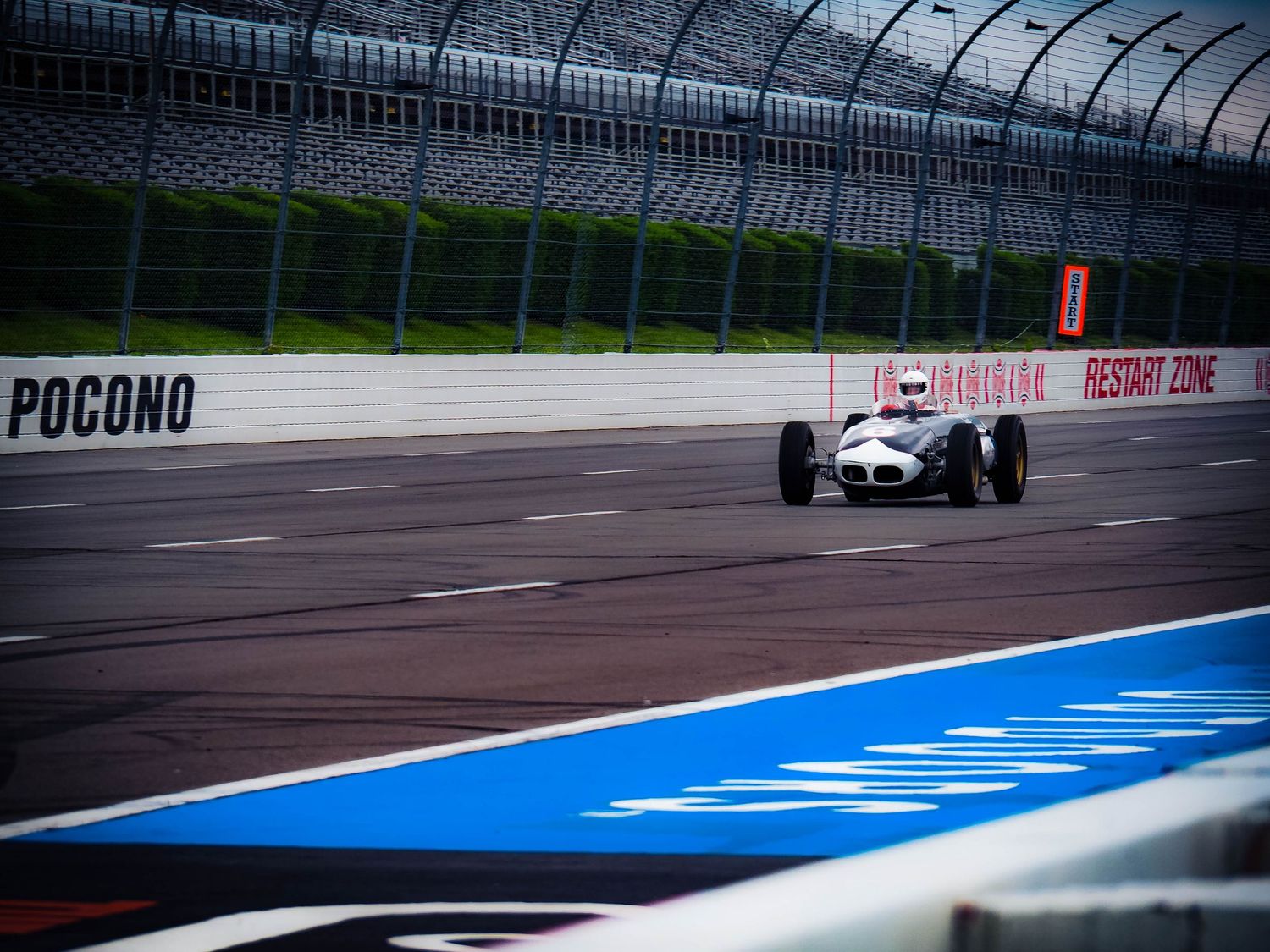 Race cars speed around the curved track at Pocono Raceway during a high-speed motorsport competition.