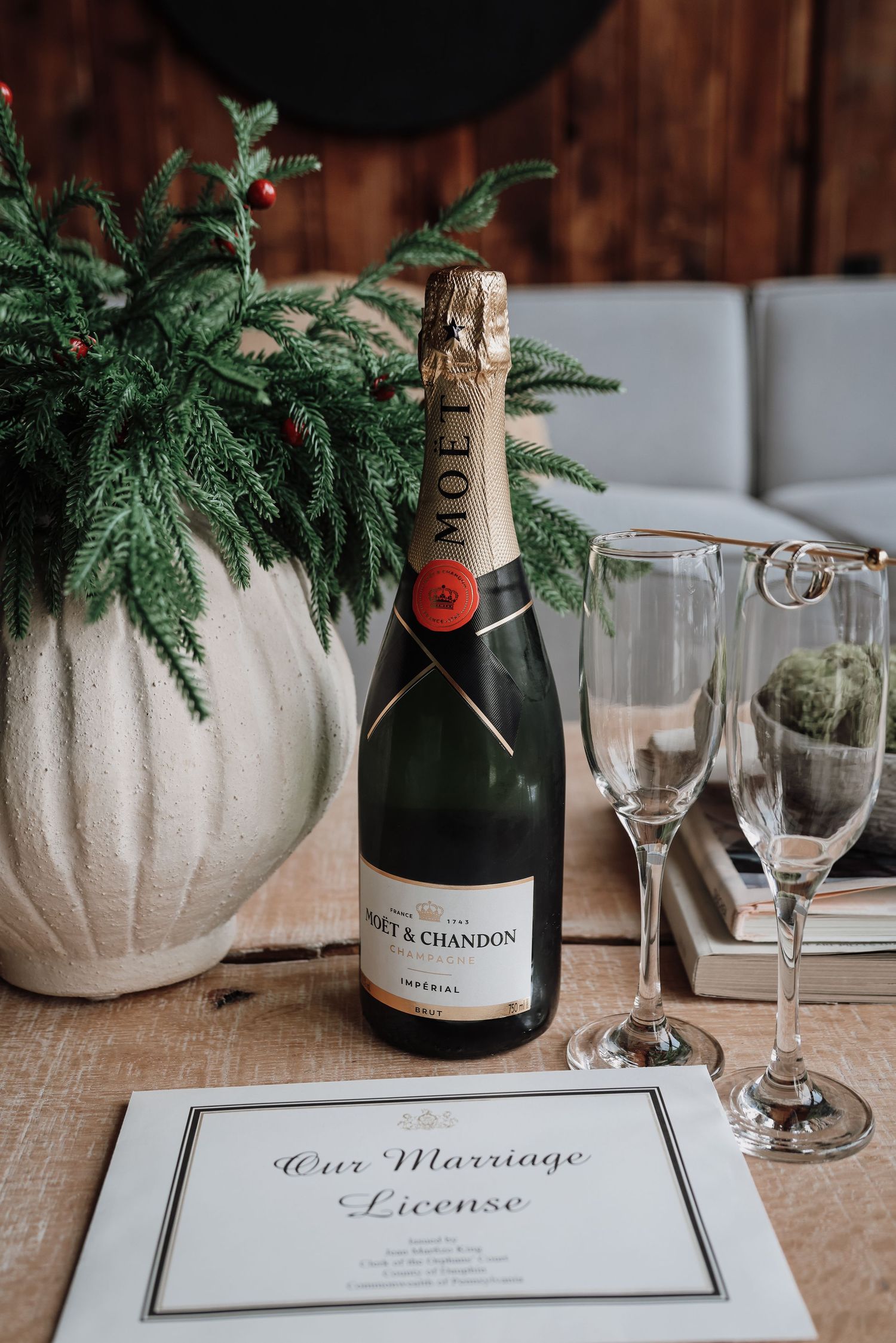 Wedding ceremony details with Moët & Chandon champagne bottle, crystal glasses, and white ceramic vases with evergreen sprigs.