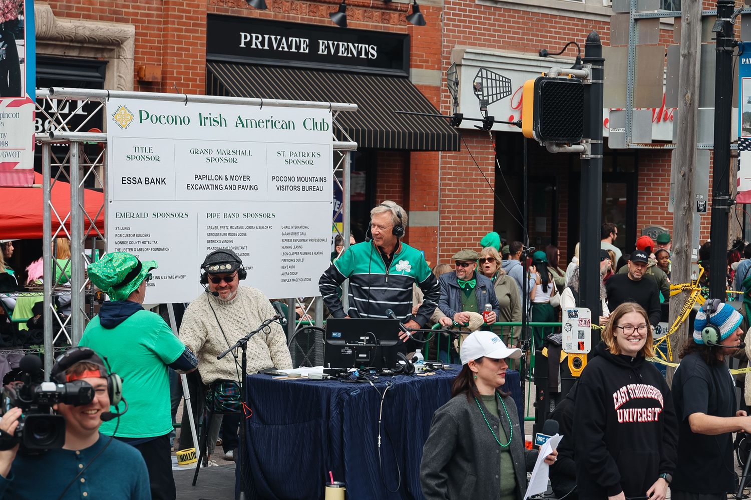 DJ performing at Pocono Irish American Club outdoor St. Patrick's Day parade event on a busy street.