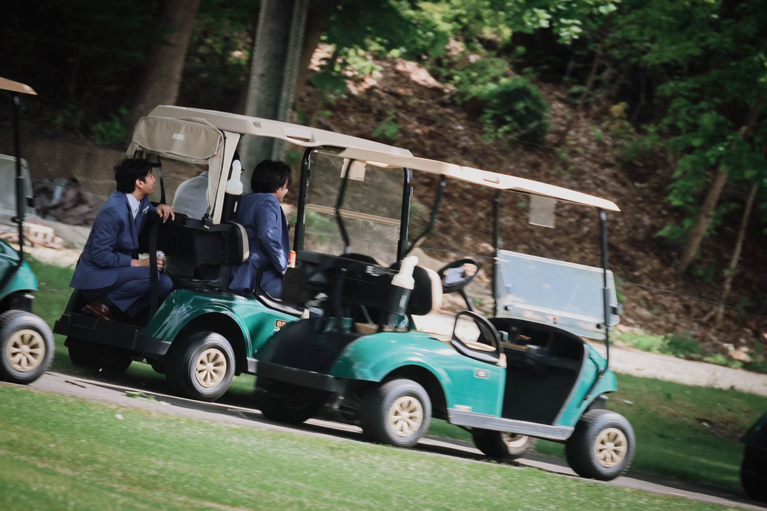 Two people riding a green golf cart on a lush golf course surrounded by trees.