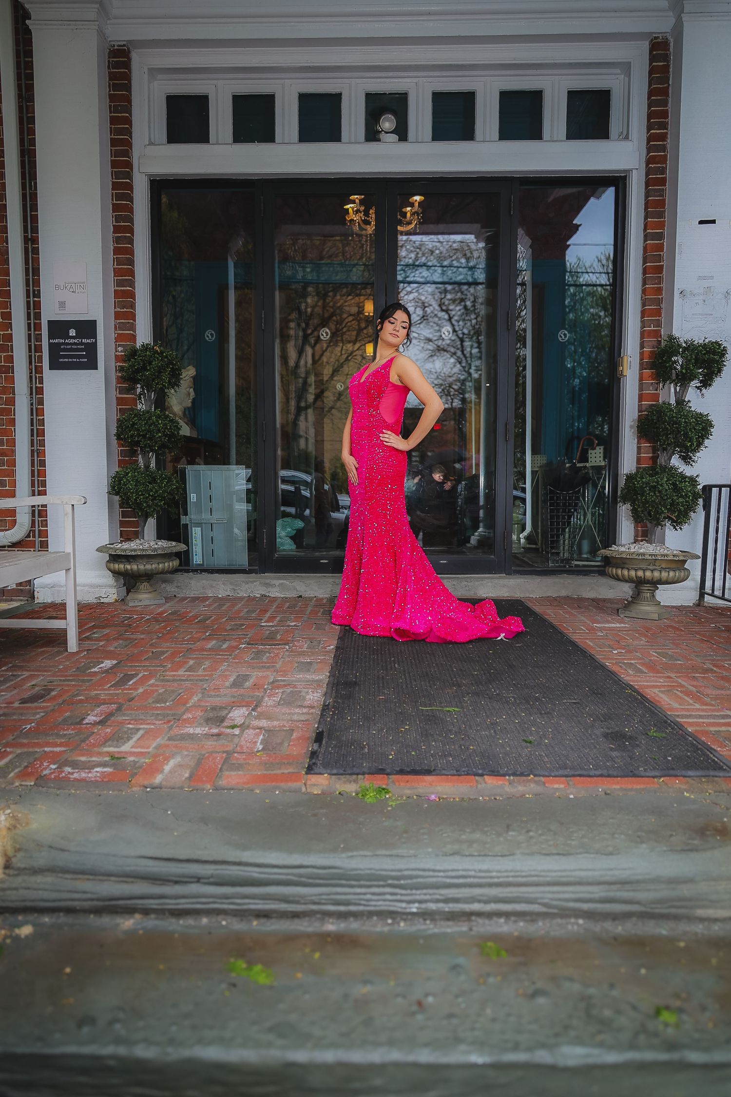 Woman in a stunning hot pink sequin mermaid gown posing at elegant brick building entrance.