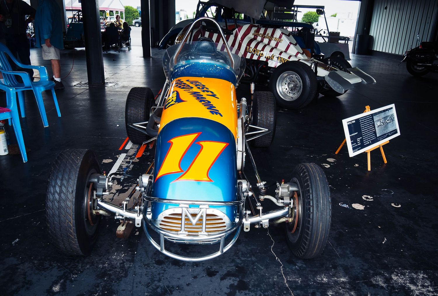 Vintage racing car details showing blue and yellow paint schemes and chrome components at a motorsport event.
