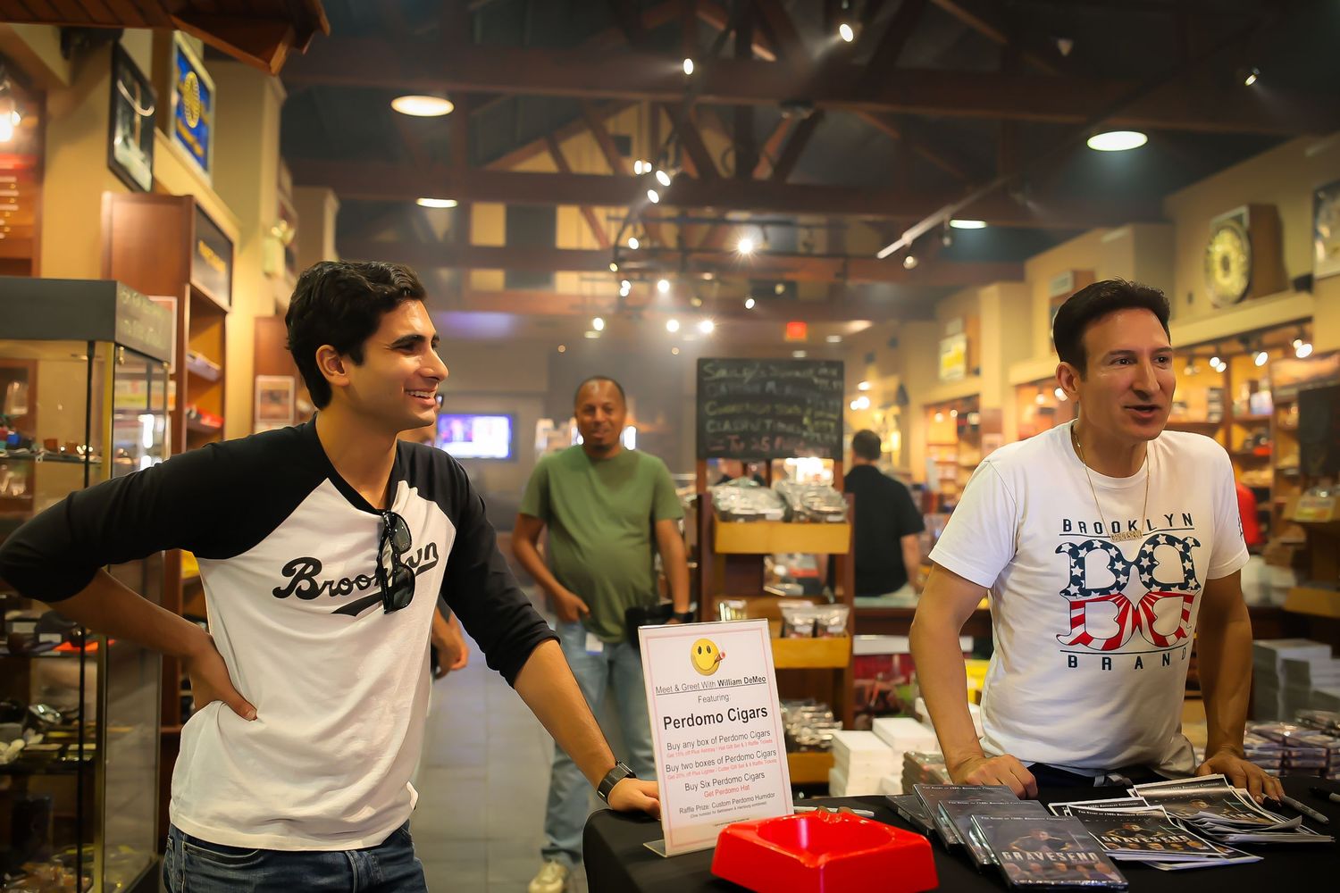 A group of people gather around a table in a casual restaurant setting with dim lighting and wall decorations.