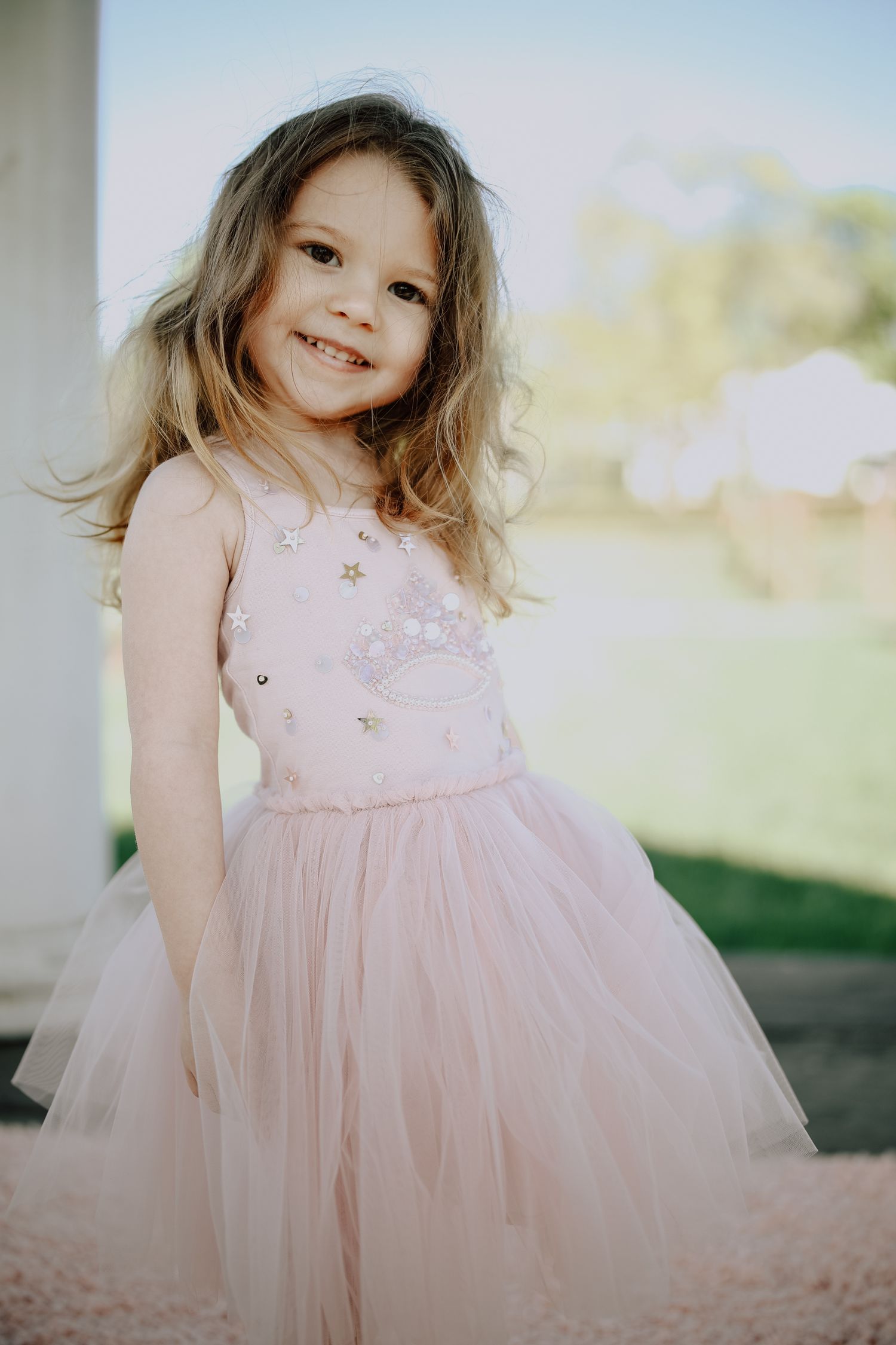 A young child in a pink tulle dress twirls and plays outdoors in a series of candid portraits.