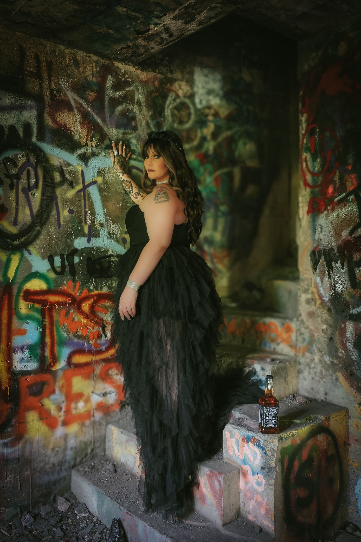 A figure in a flowing black dress poses against graffiti-covered walls in an abandoned urban setting.