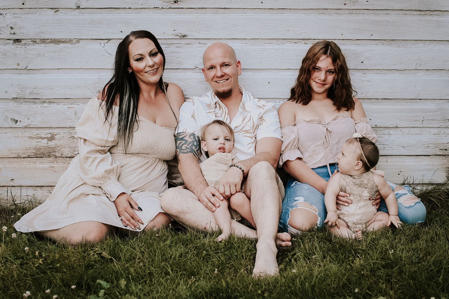 Family relaxing together on grass against rustic white wooden wall background.