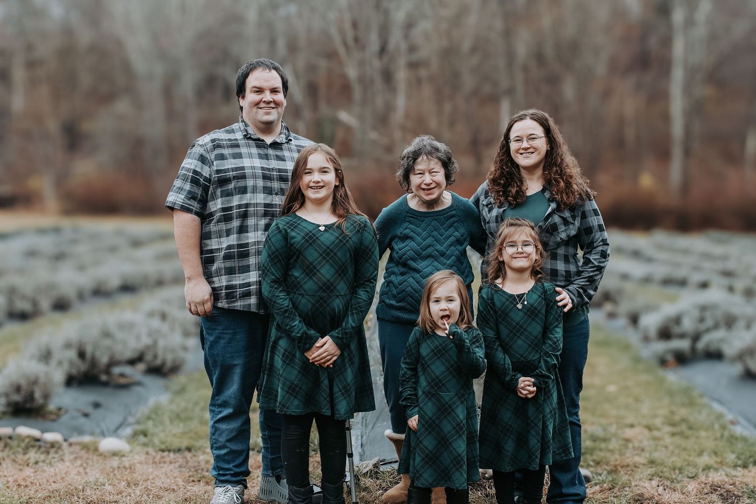 A family in coordinated plaid and dark green outfits poses together outdoors on a rocky hillside during autumn.