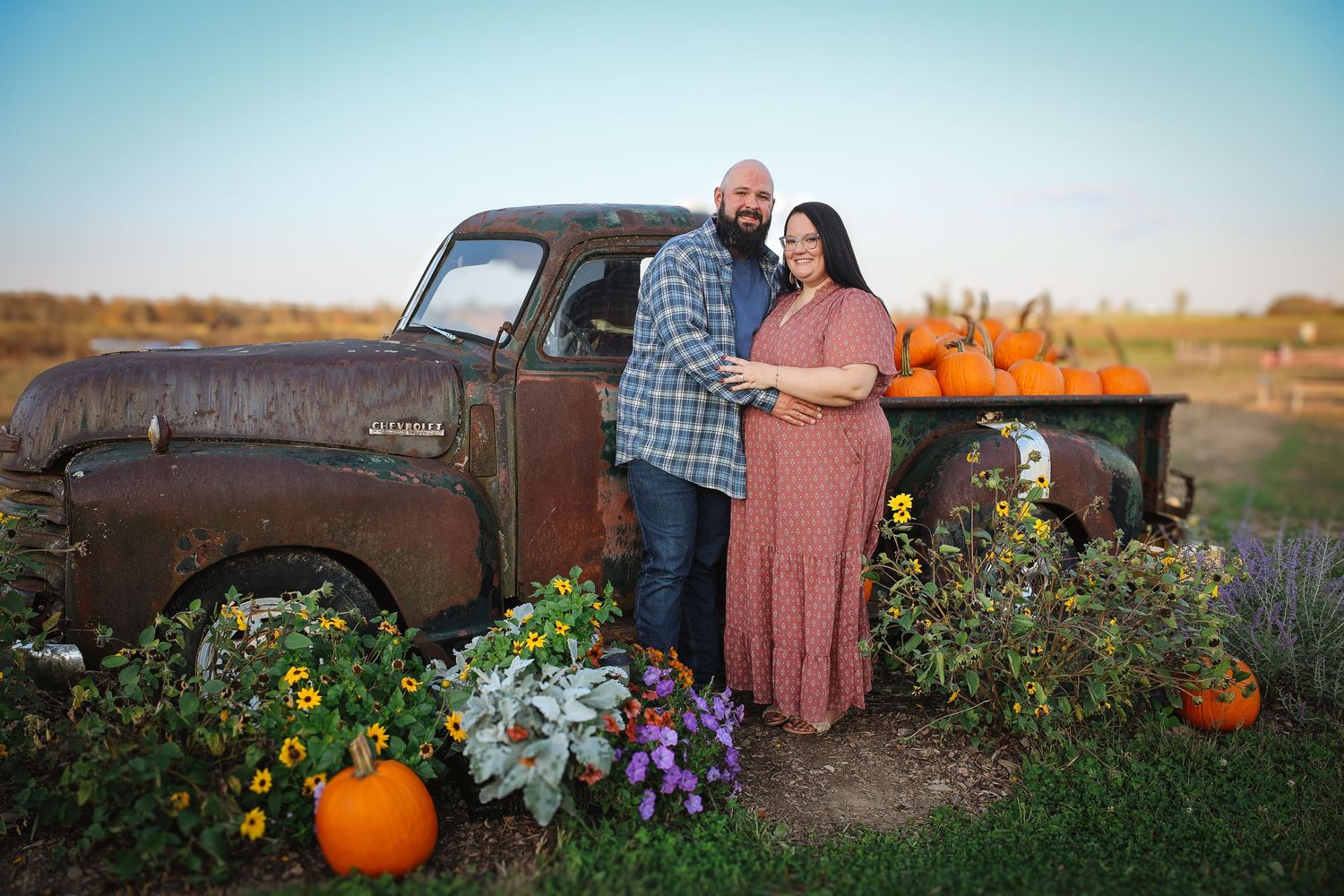 A rustic vintage pickup truck decorated with fall pumpkins and flowers in a country field setting at sunset.