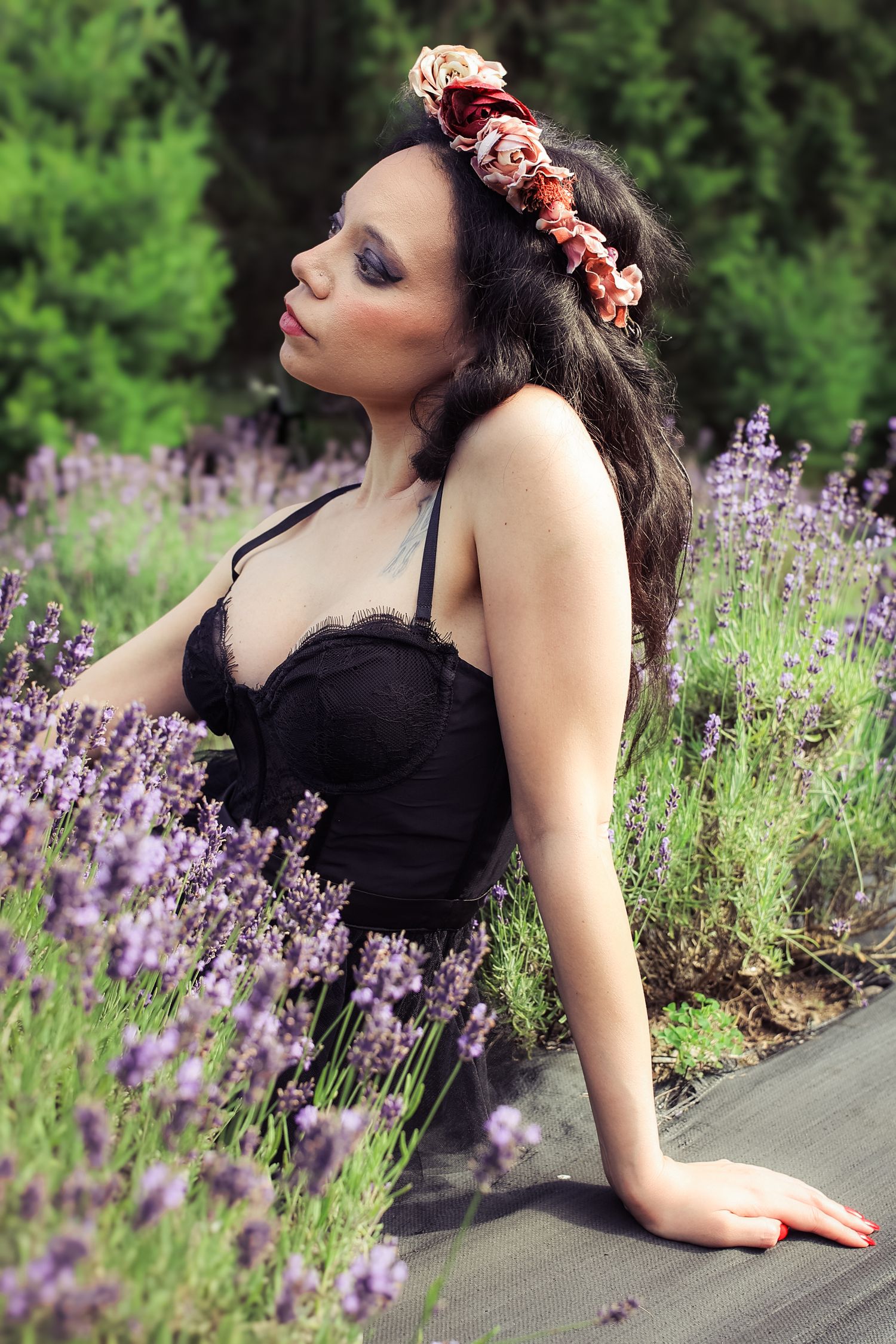 A figure in a black dress poses gracefully among blooming lavender flowers in a garden setting.