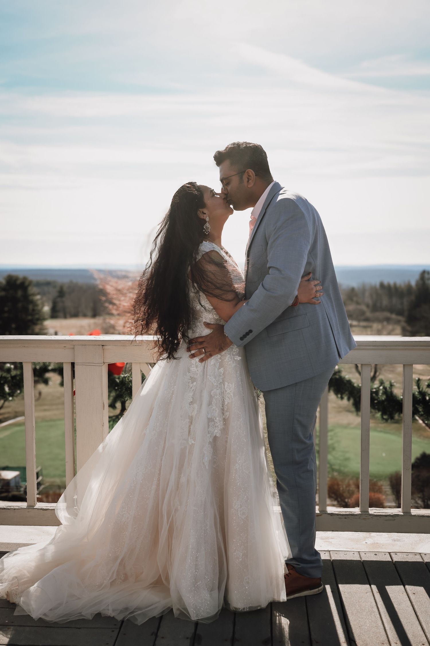 A couple in wedding attire share romantic moments on a balcony overlooking scenic countryside views.