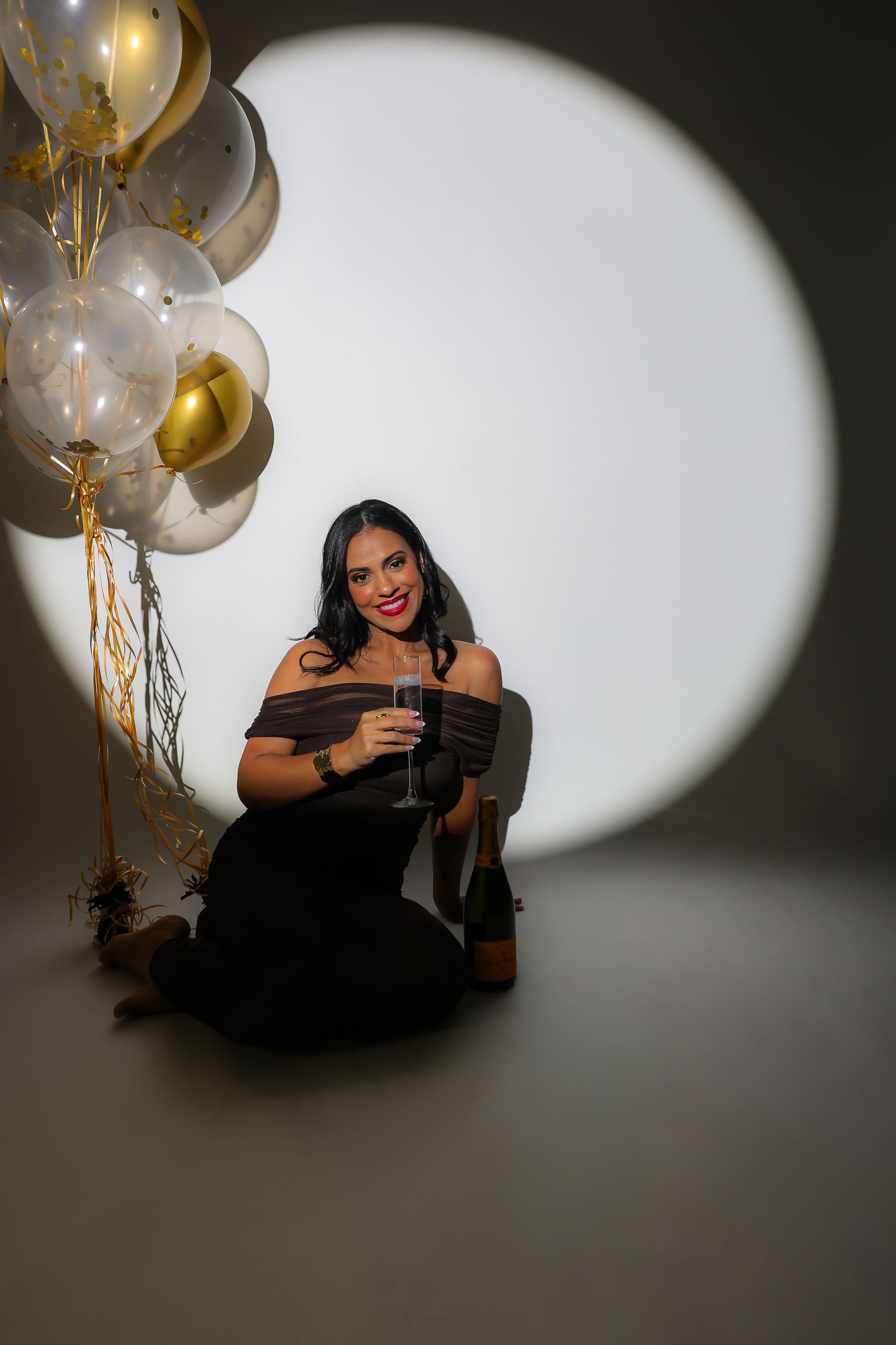Model in a black dress celebrates with gold and silver balloons against a dramatic spotlight background.