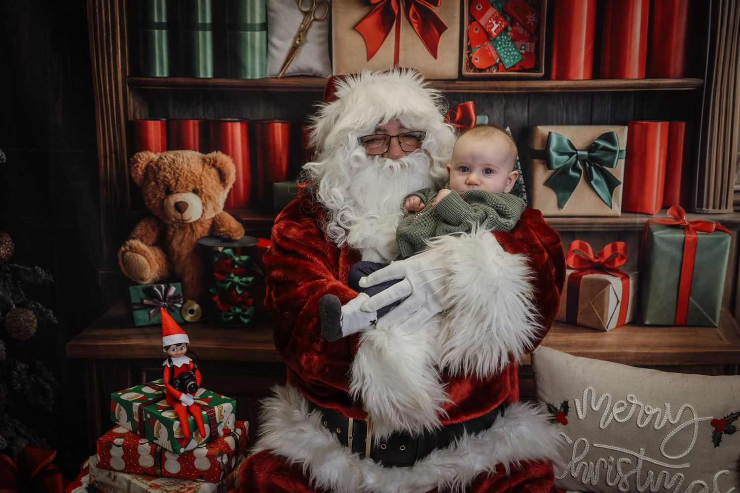 A Christmas-themed photo studio setup with red decorations, wrapped presents, and white fluffy accents for holiday portraits.