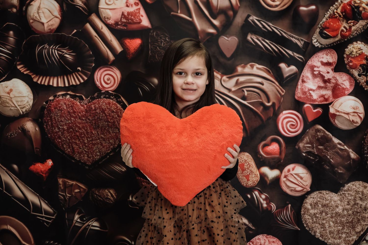 Assorted chocolate candies and heart-shaped treats arranged on dark background with red accents for Valentine's Day.
