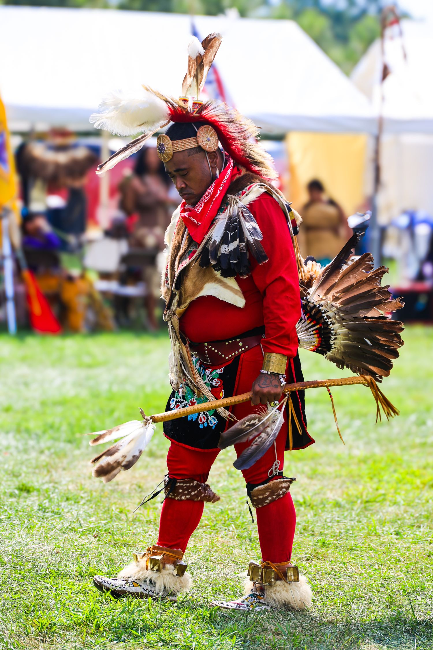 Native American dancers in traditional red regalia perform traditional dance movements at an outdoor powwow celebration.