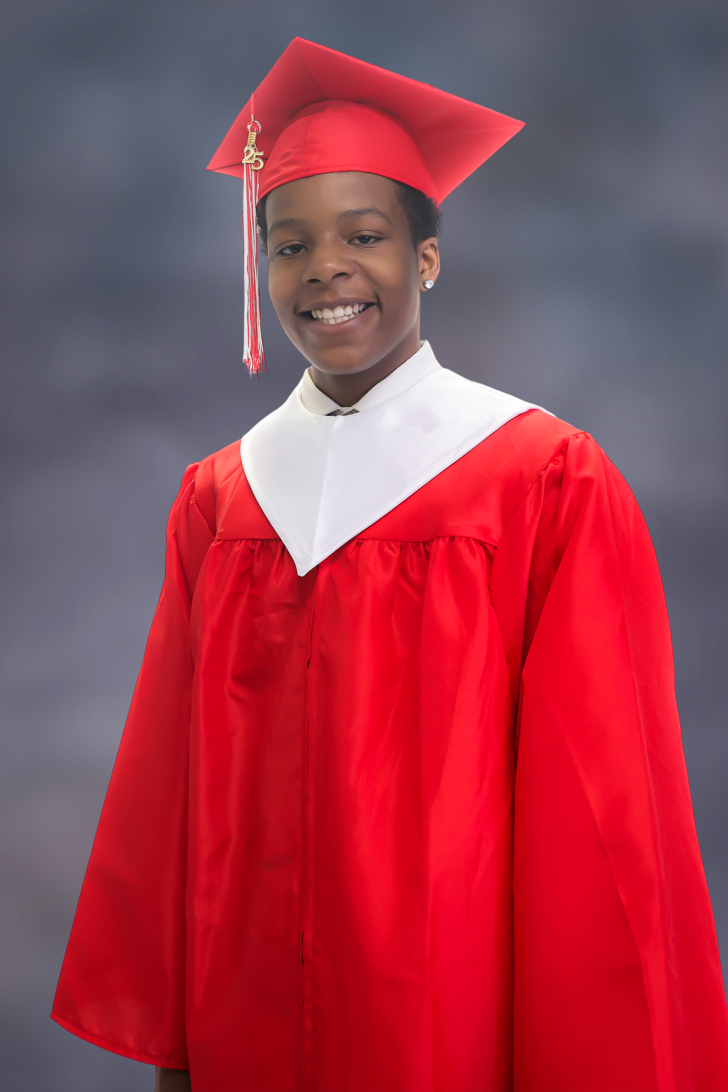 Graduate wearing bright red cap and gown poses in front of grey backdrop for portrait photos.