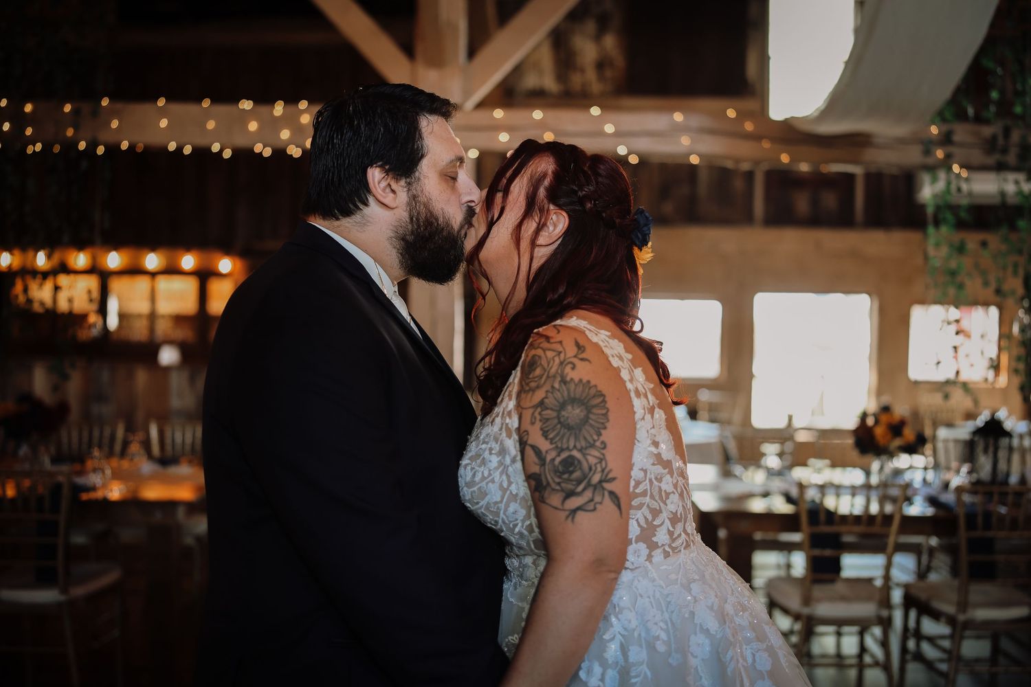 A romantic wedding couple shares an intimate dance under twinkling lights in a rustic barn venue.