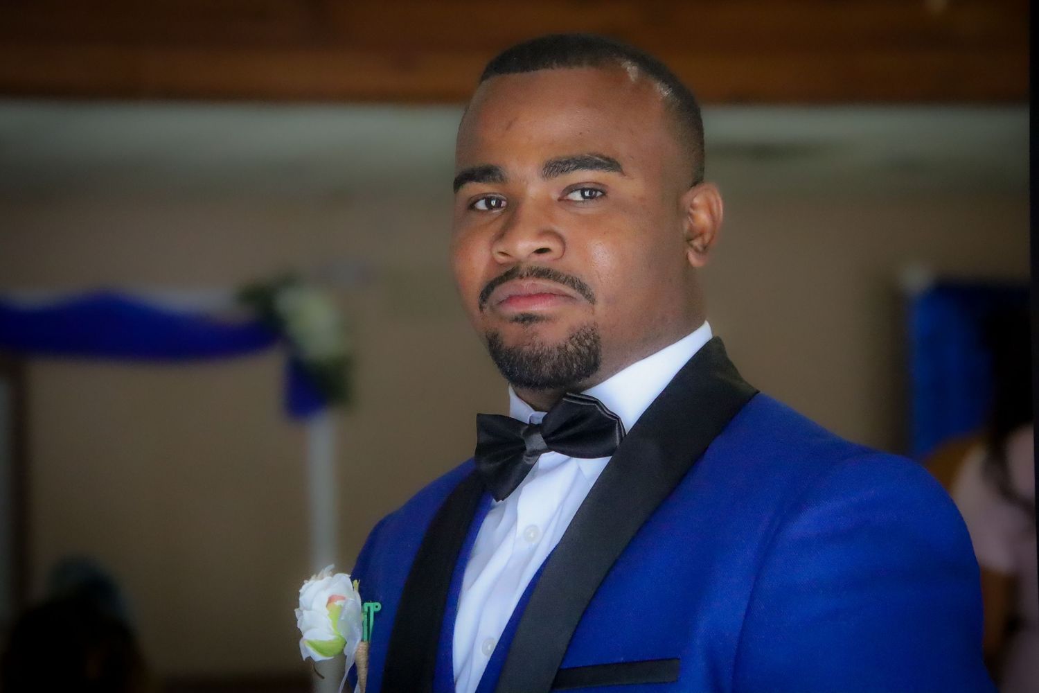 A person wearing a royal blue tuxedo jacket with black bow tie and white boutonniere at a formal event.